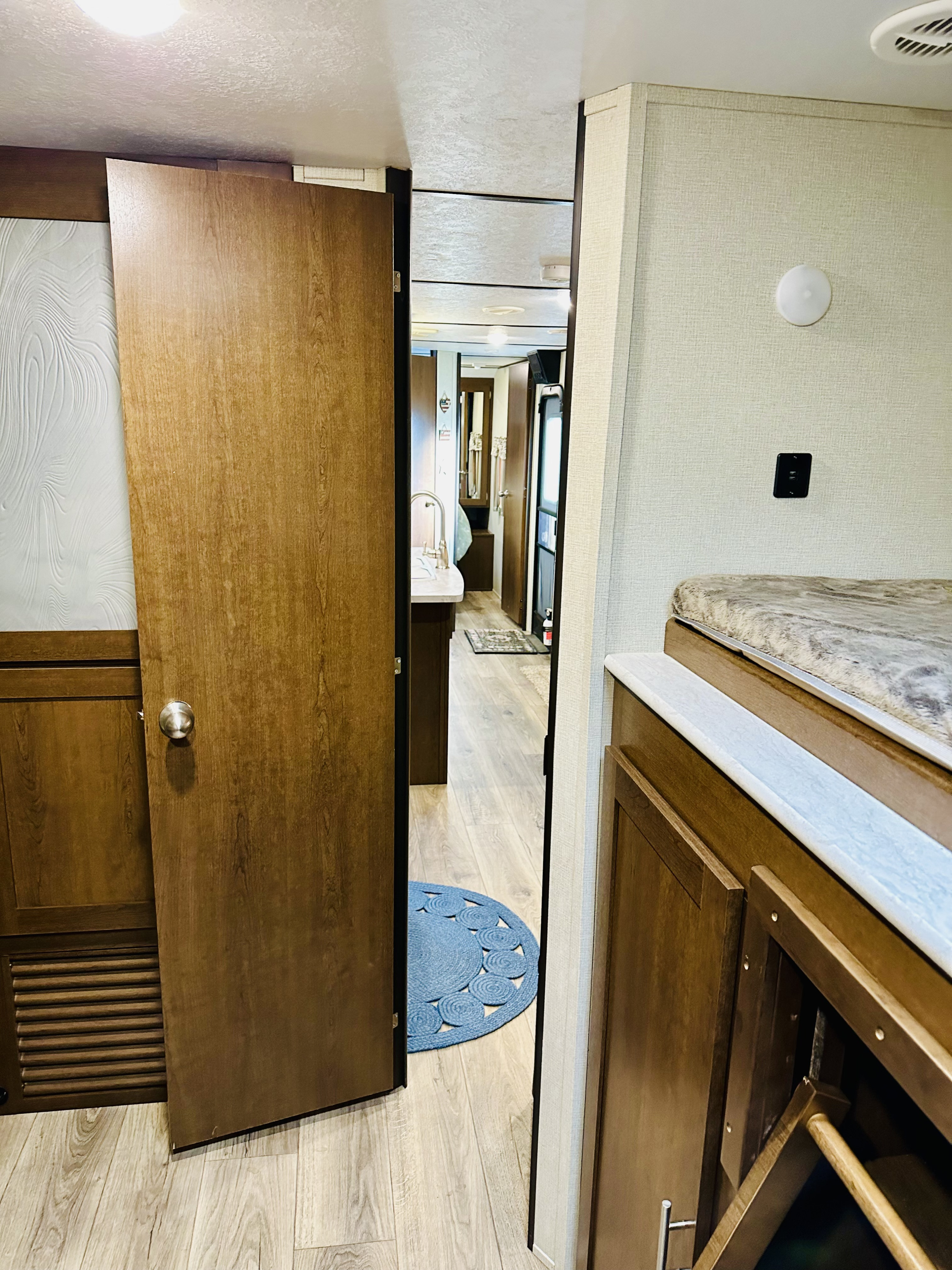 An RV rental interior showing a hallway, kitchen area, and a bunk bed. Features wood accents and light walls.. Forest River Wildcat 2019