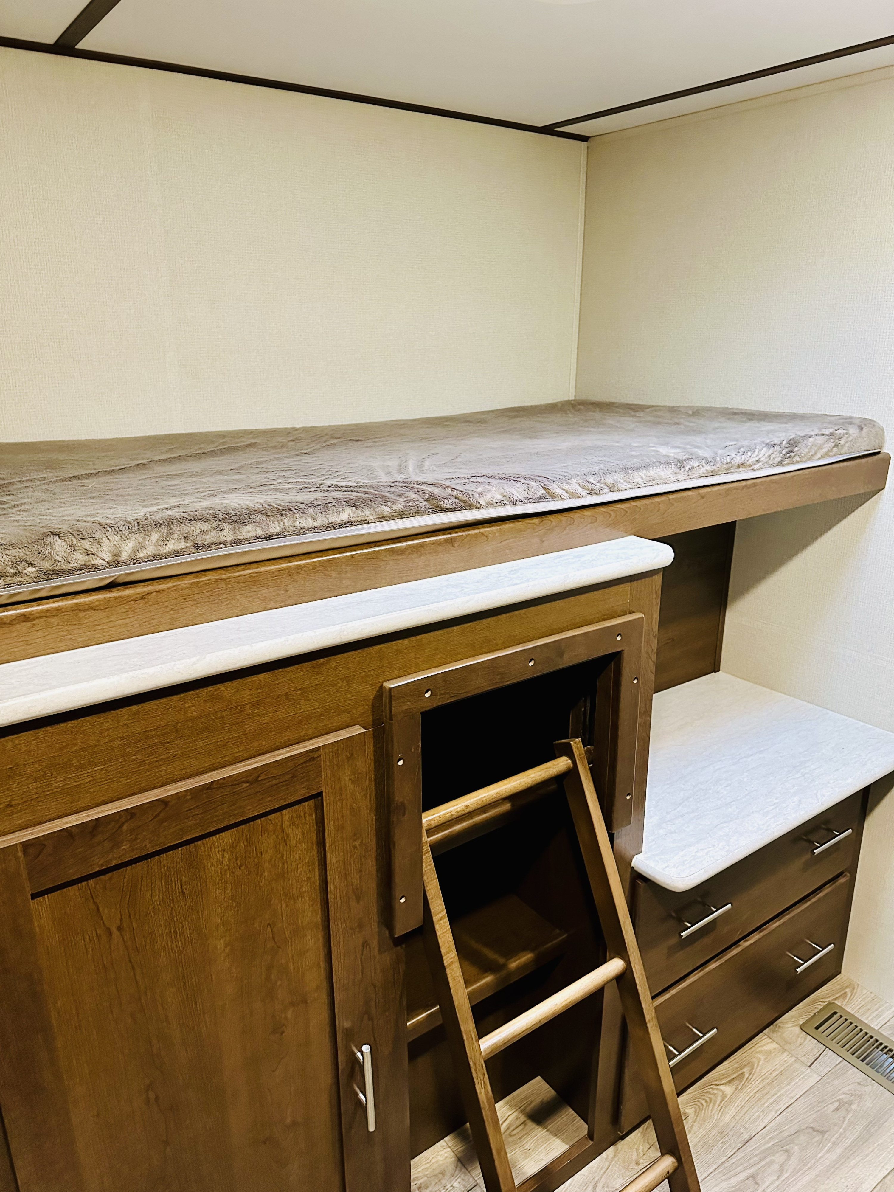 RV rental interior: A top bunk bed above wooden cabinets with a ladder accessing a storage cubby and drawers. Compact living.. Forest River Wildcat 2019