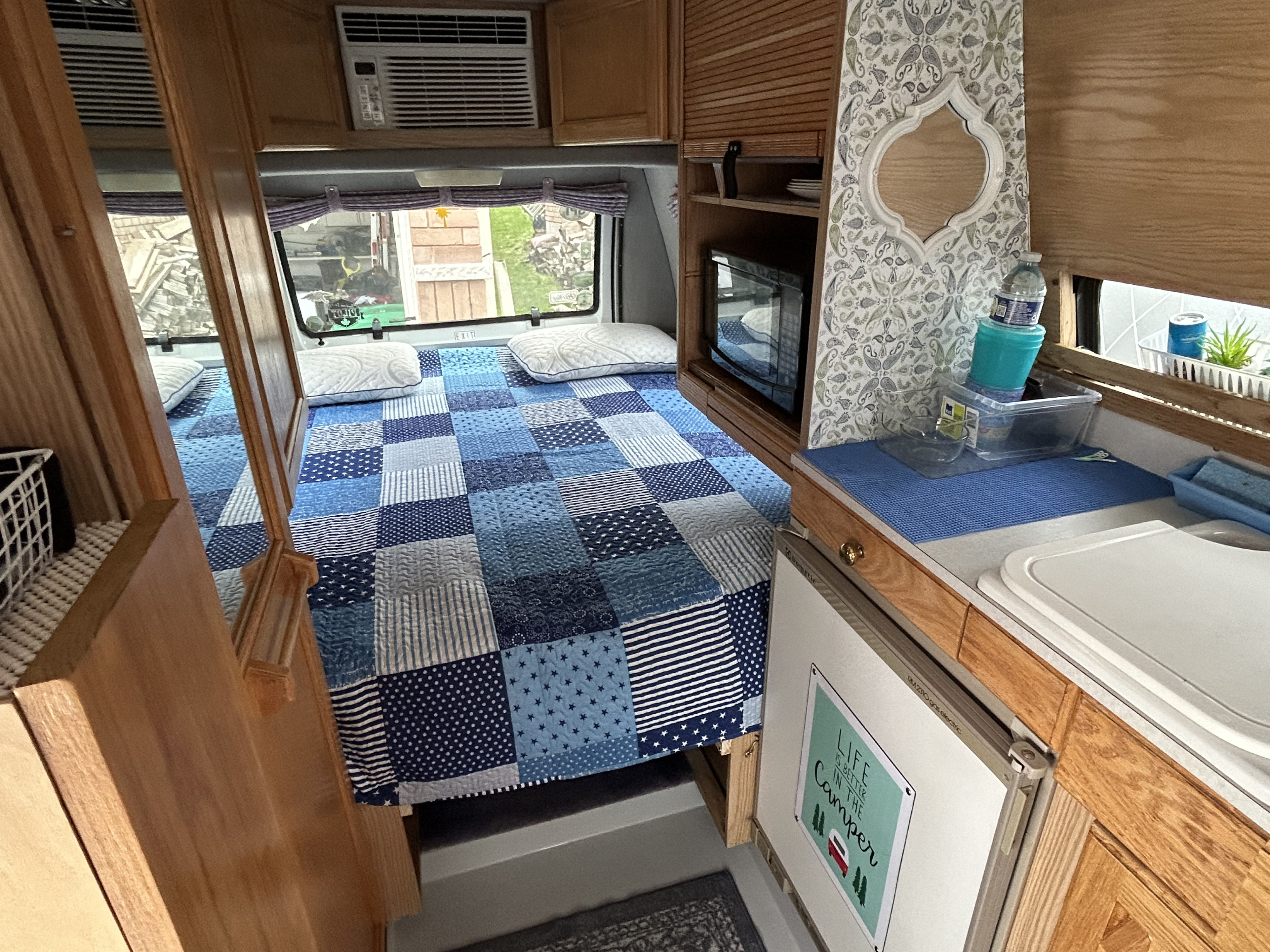 Inviting RV rental interior with a blue patchwork bed, compact kitchen, microwave, and wood finishes throughout.. Roadtrek 190 Popular 1997