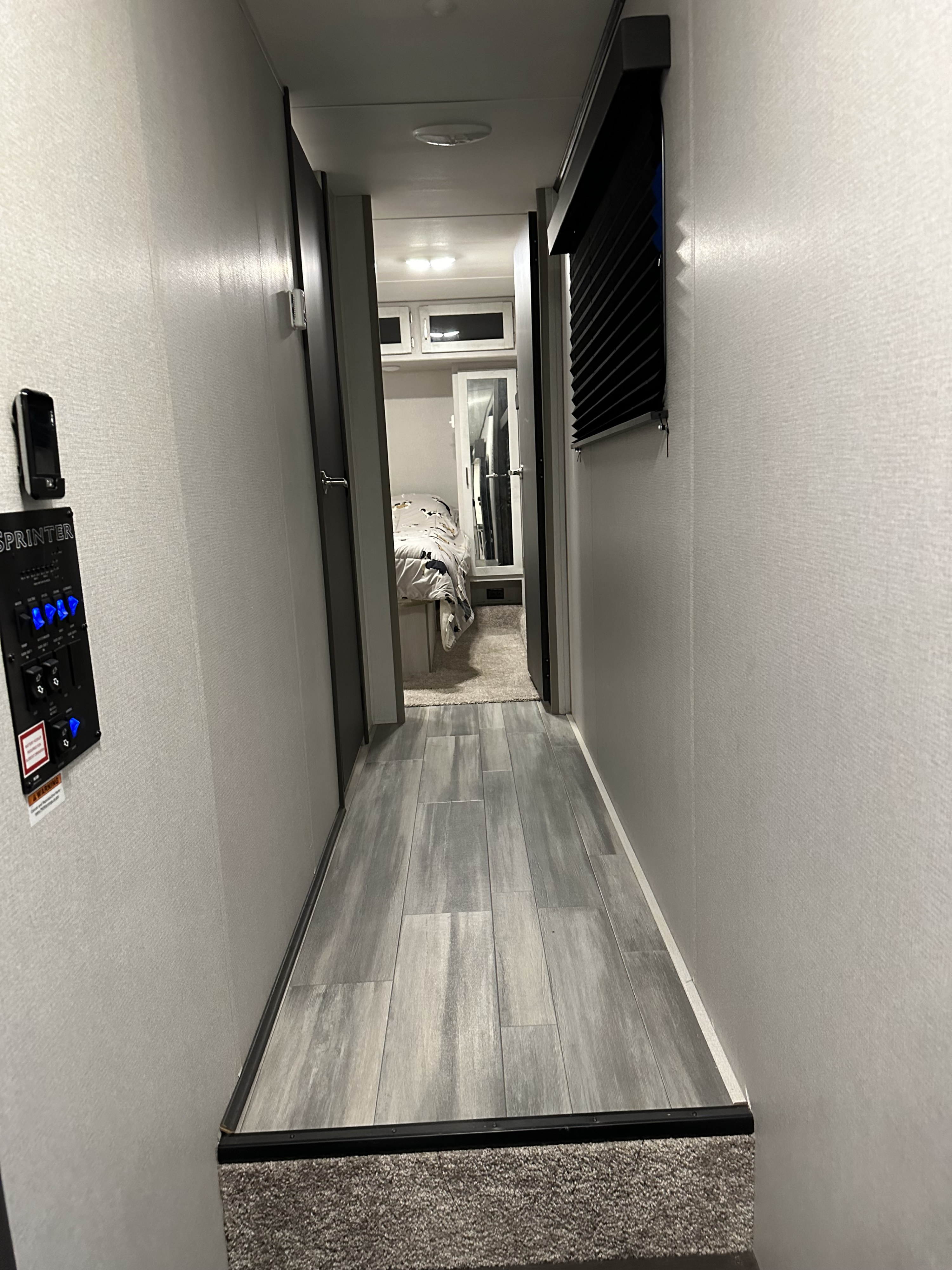 RV rental: A modern interior hallway with wood-look floor leads to a cozy bedroom. Control panel on left.. Keystone Sprinter 2021