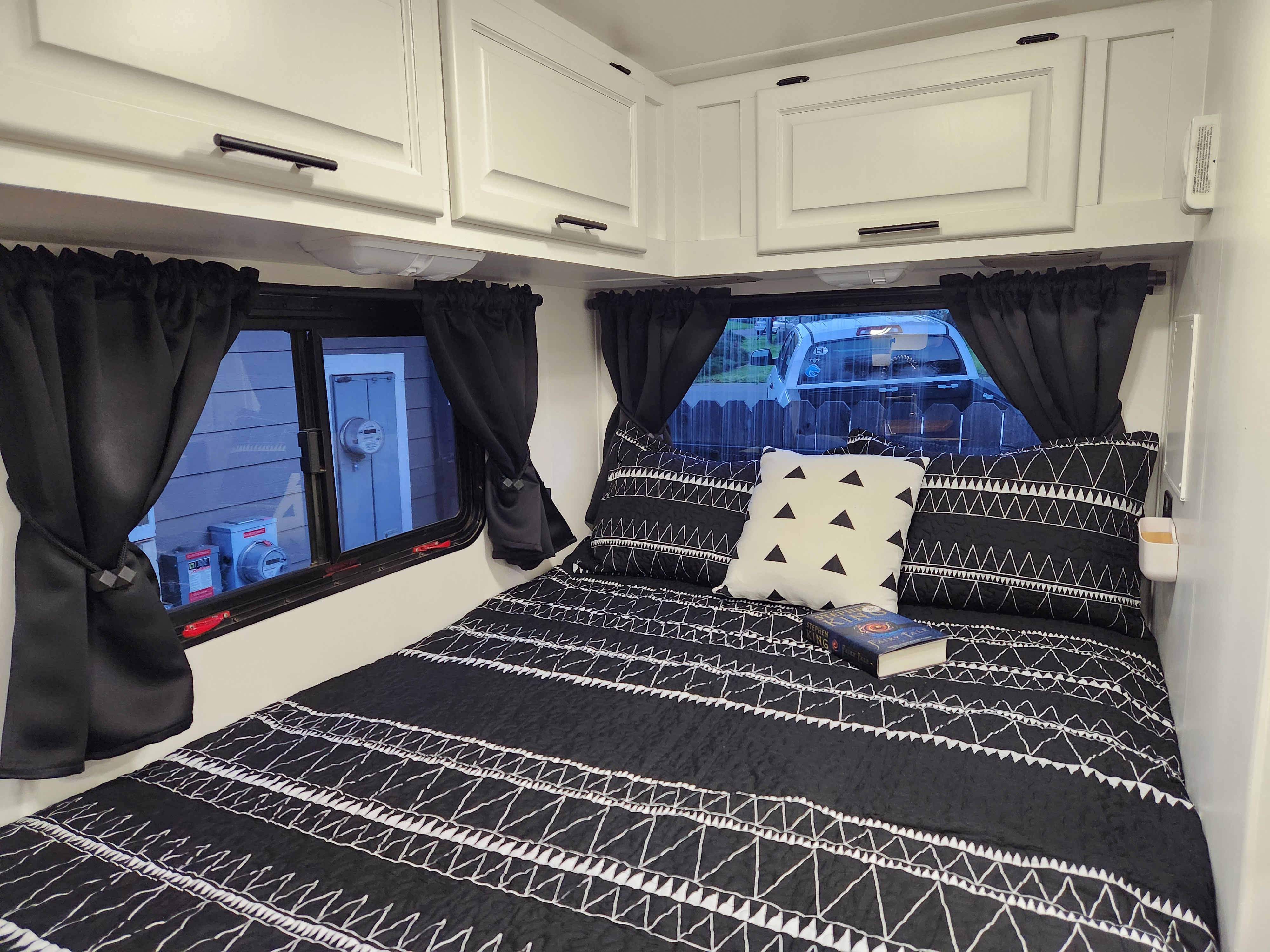 RV rental bedroom: a cozy space with a black & white bed, tie-back curtains on windows, and white overhead cabinets.. Four Winds Majestic 2008