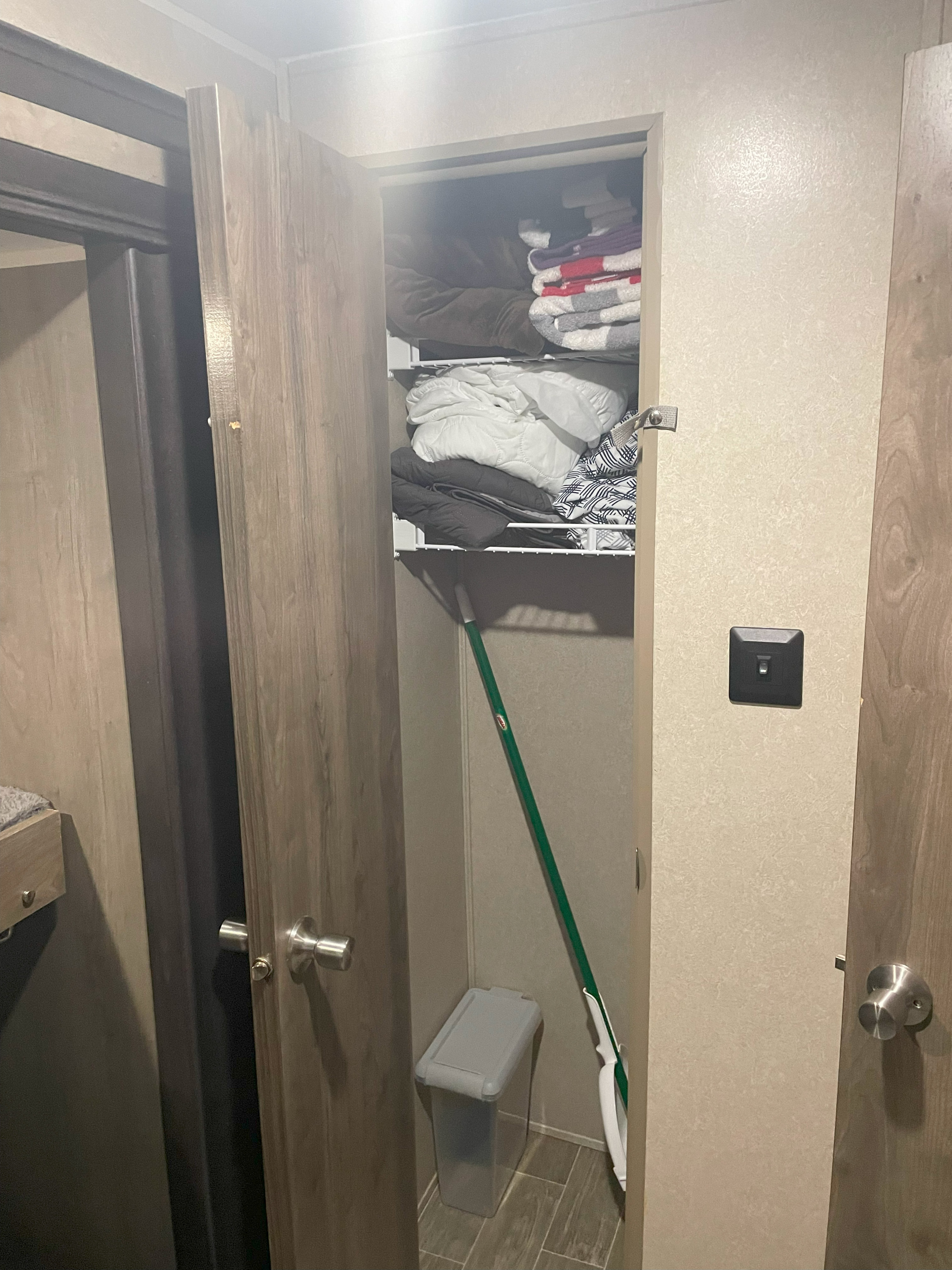RV rental closet provides compact storage with shelves of linens, a mop, and a container on the floor. Functional space.. Palomino Puma 32BHKS 2020