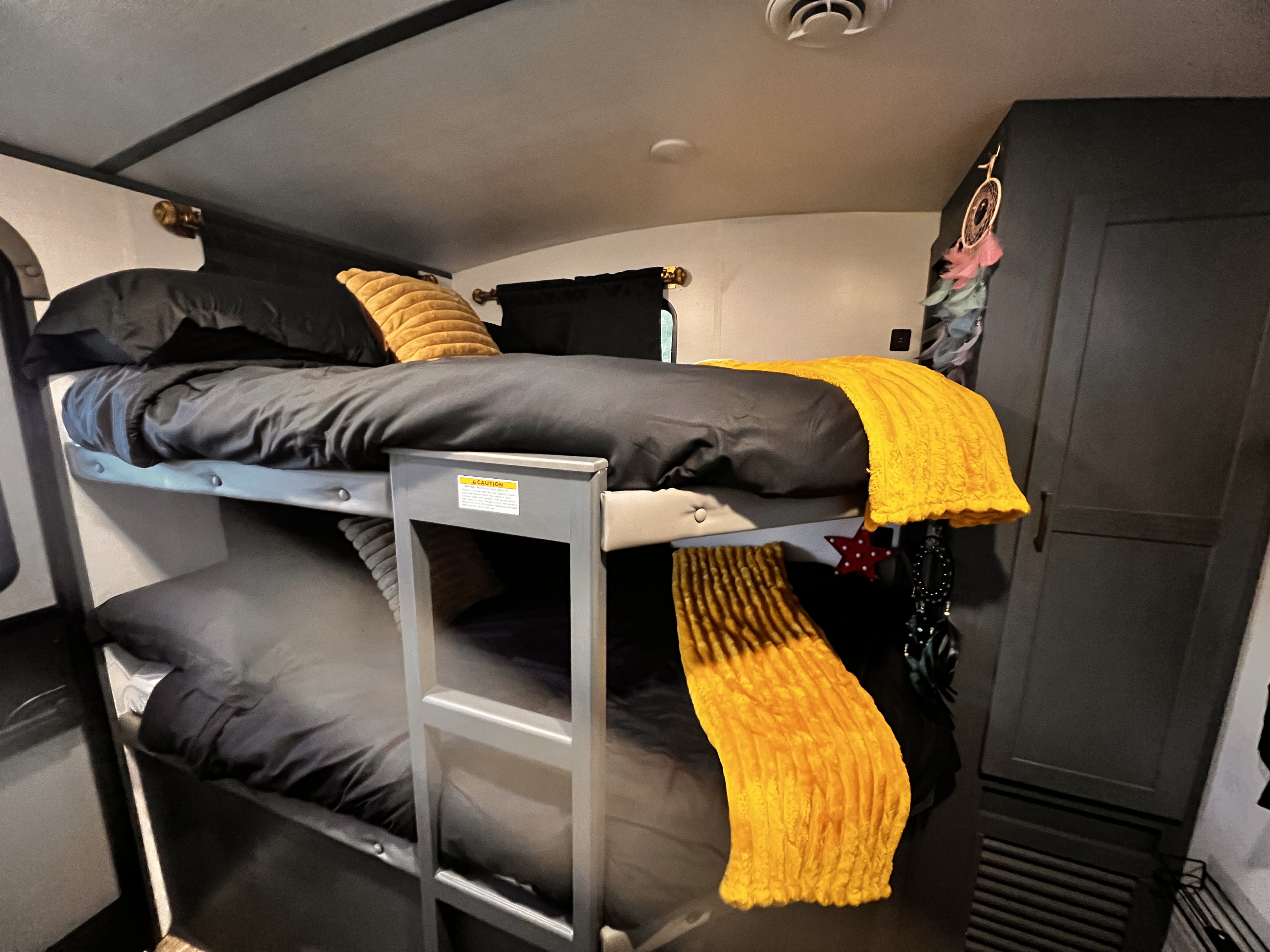 RV rental bunk beds: dark bedding, bright yellow throws, and ladder. Cozy sleeping area with storage in a camper.. Keystone RV Bullet Ultra Lite 2022