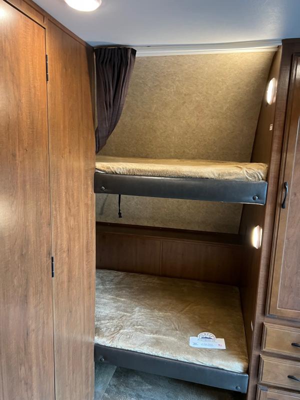 View inside an RV rental showing a wood-paneled interior with stacked bunk beds, featuring soft mattresses and individual lights.. Jayco Jay Feather 2016