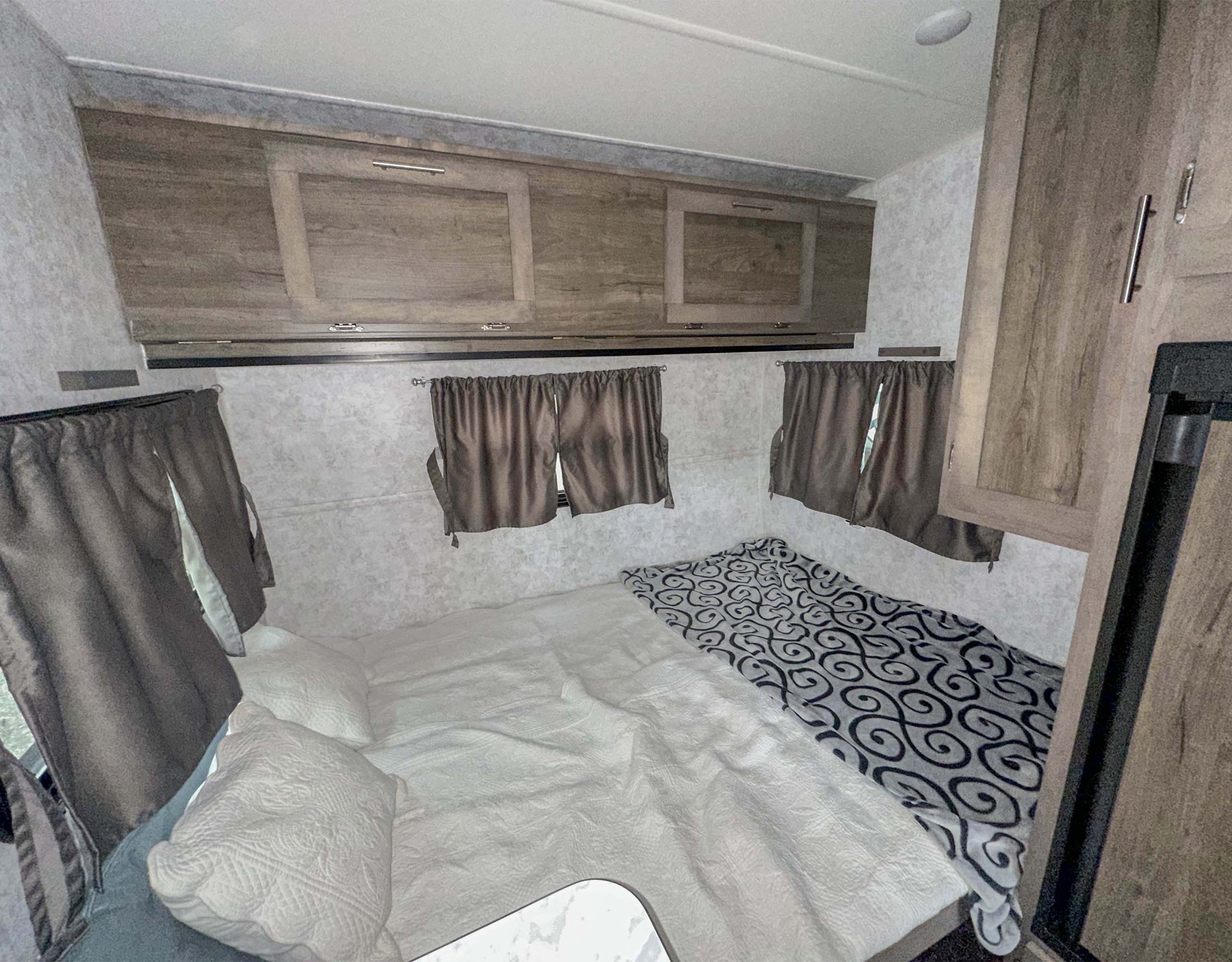 RV rental interior: a cozy bedroom with a comfortable bed, overhead cabinets, and curtained windows.. Prolite Evasion 2021