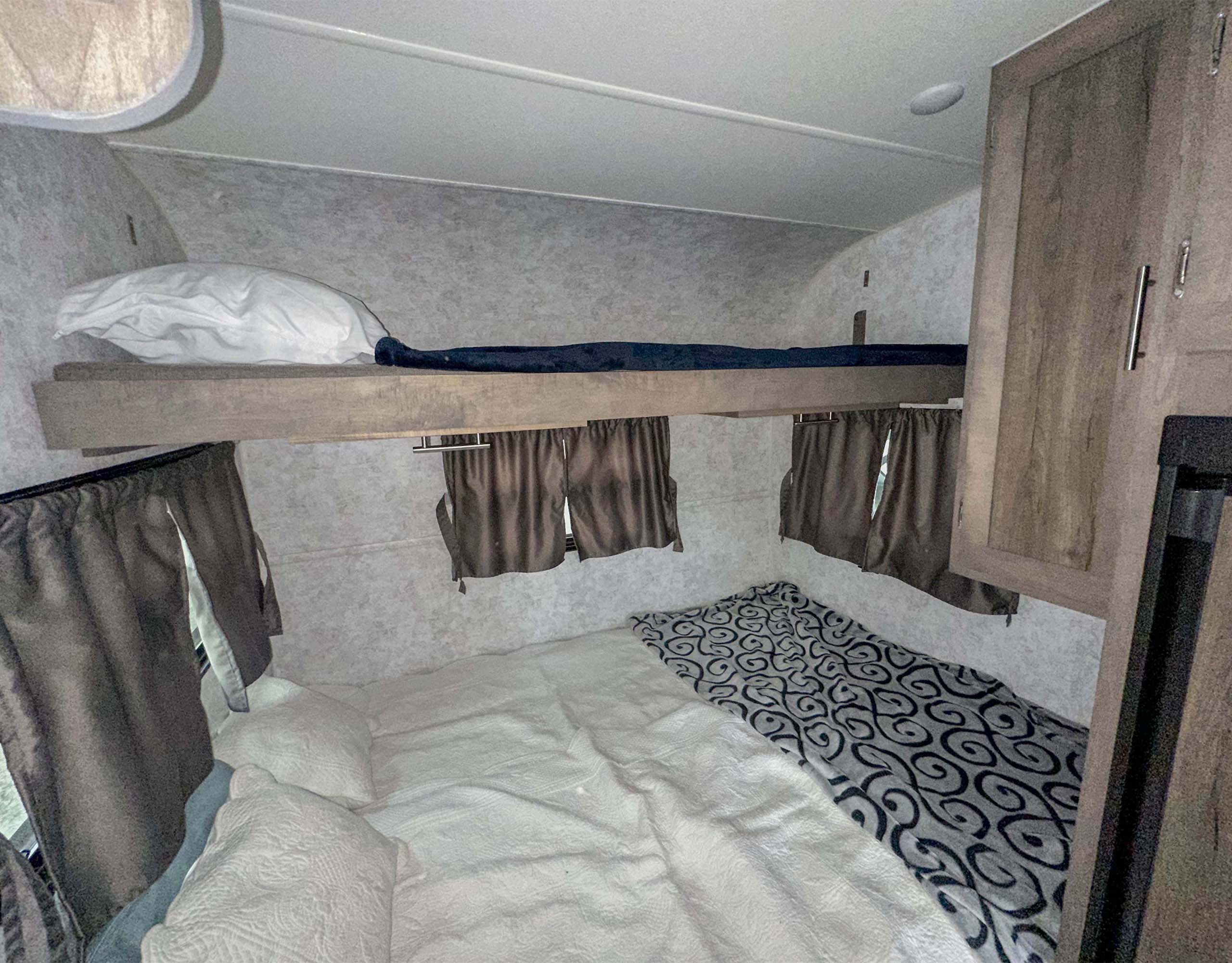 Cozy RV rental bedroom showing bunk beds, white and patterned bedding, and small windows with curtains.. Prolite Evasion 2021