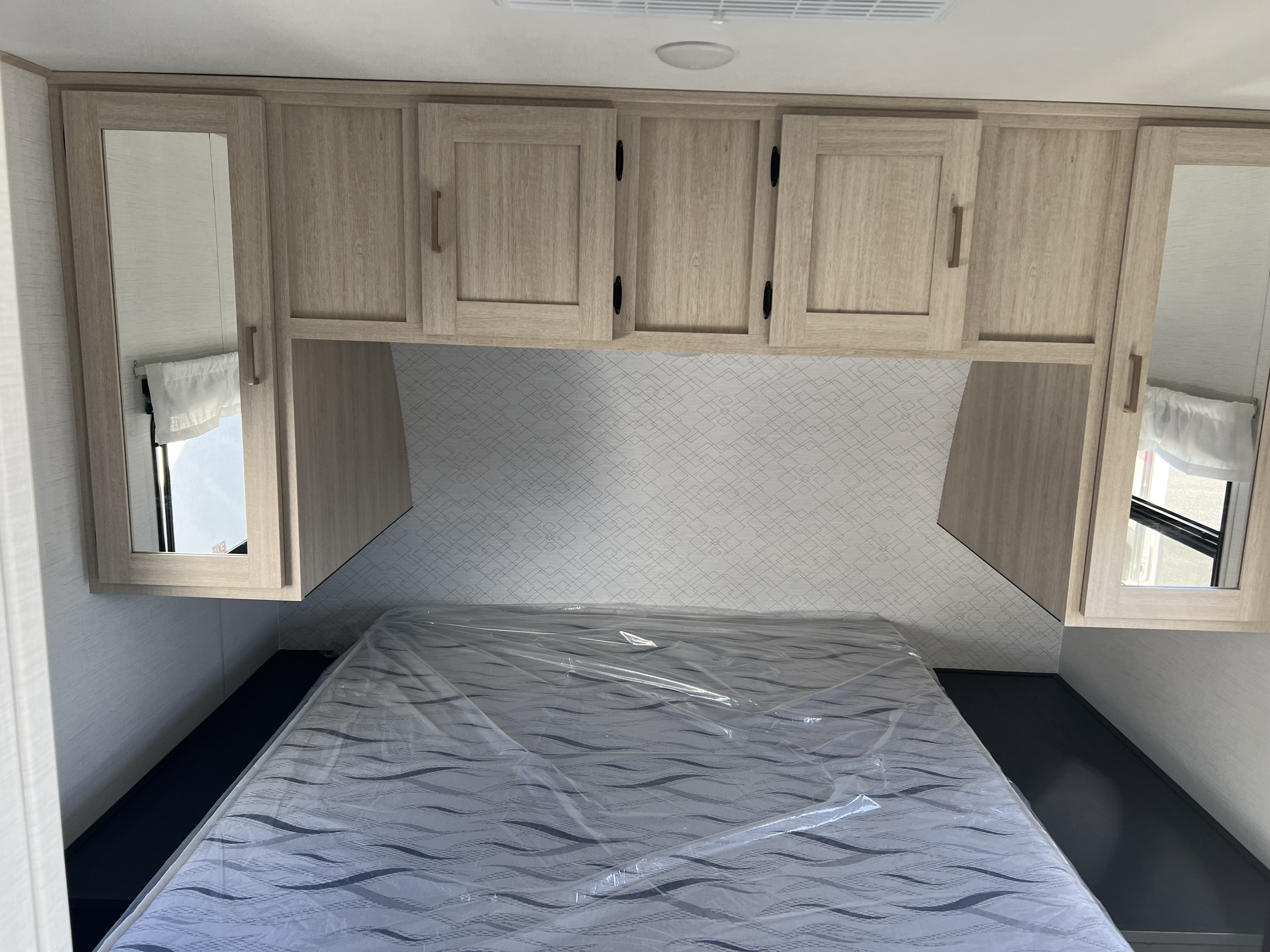 Ready for your trip: This RV rental bedroom features a new mattress, mirrored overhead cabinets, and built-in storage.. Forest River avenger 2024