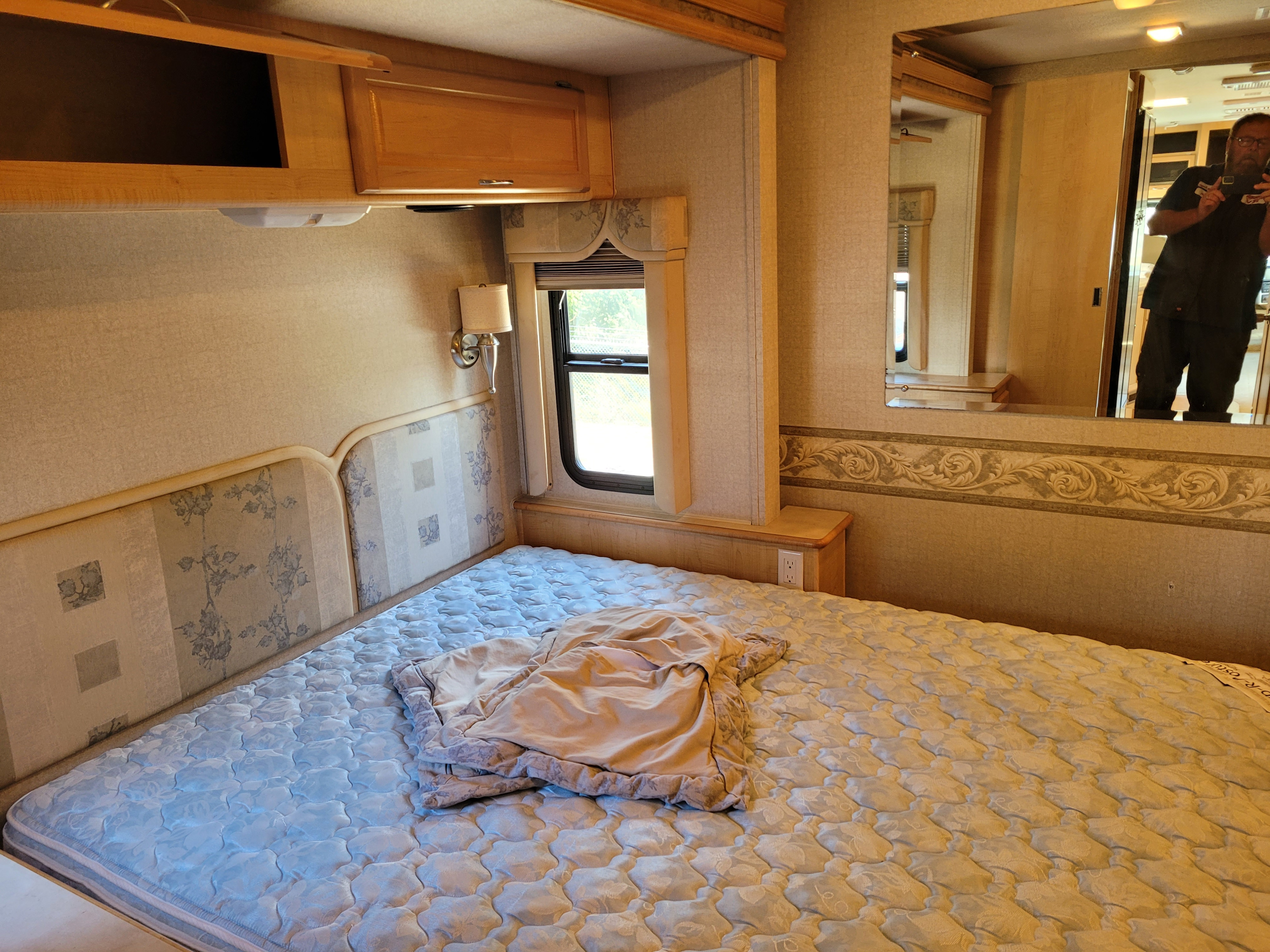 RV rental bedroom: comfortable patterned mattress, detailed headboard, wall lamp, overhead cabinets & reflective mirror.. Southwind Southwind Motorhome 2006