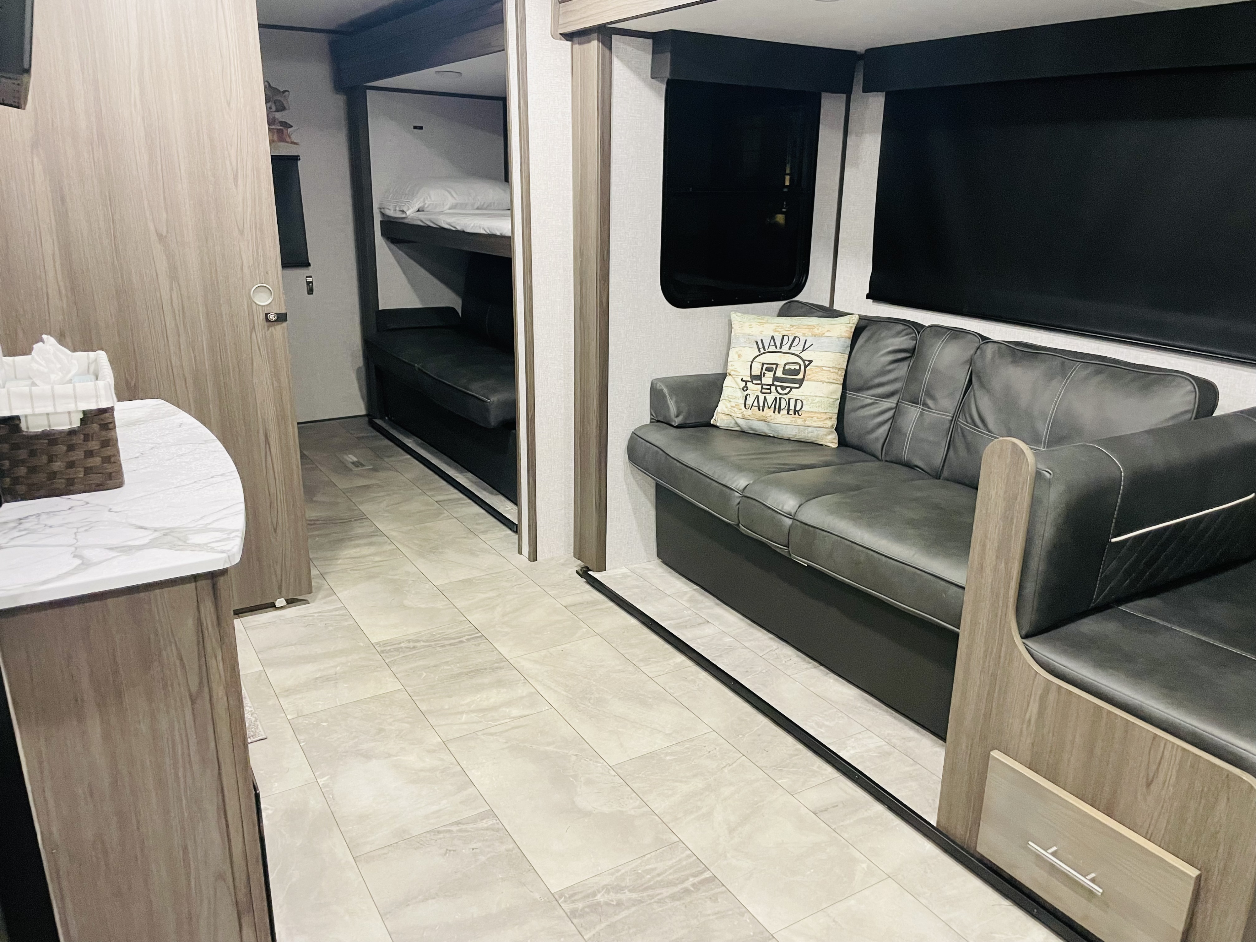 Modern RV rental interior featuring a gray faux leather couch, bunk beds, and a white marble-look counter.. Dutchmen Kodiak Ultra Lite 2021