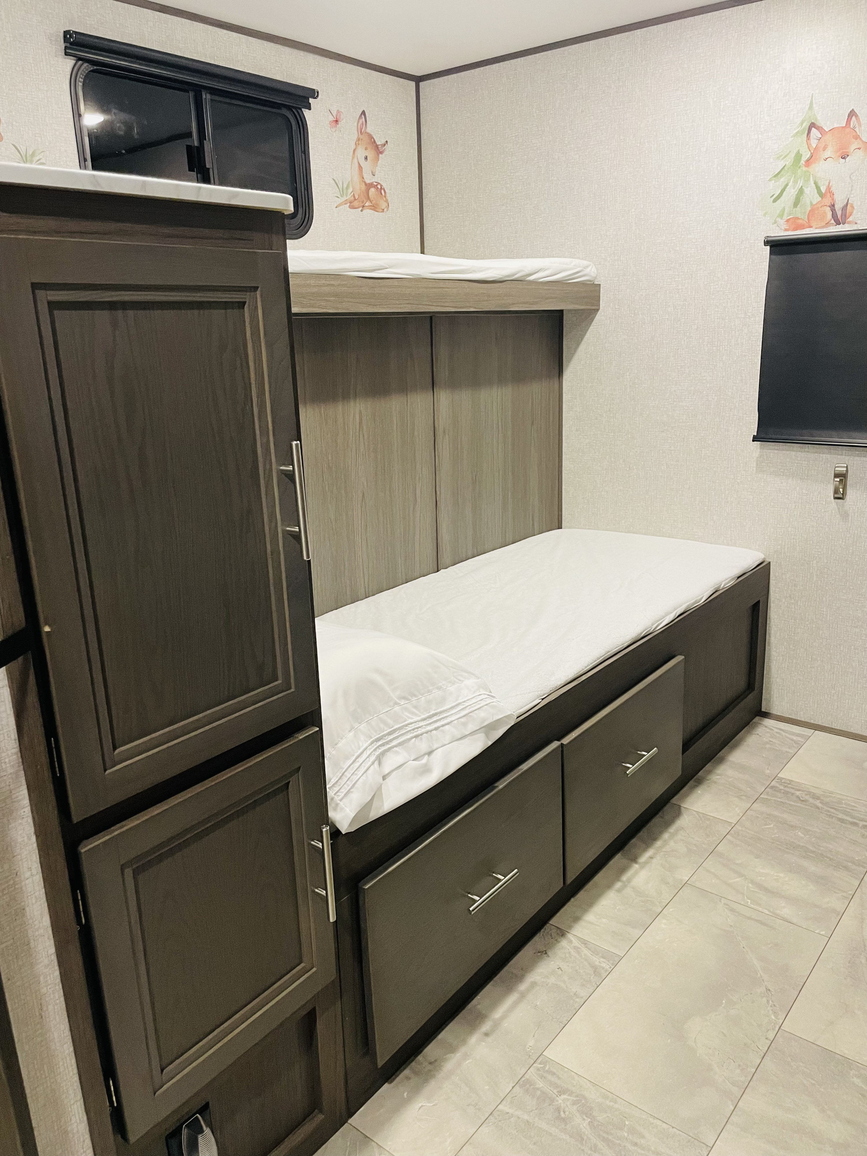 RV rental interior: cozy bunk bed area with integrated storage drawers, a wardrobe, window, and charming forest animal decals.. Dutchmen Kodiak Ultra Lite 2021
