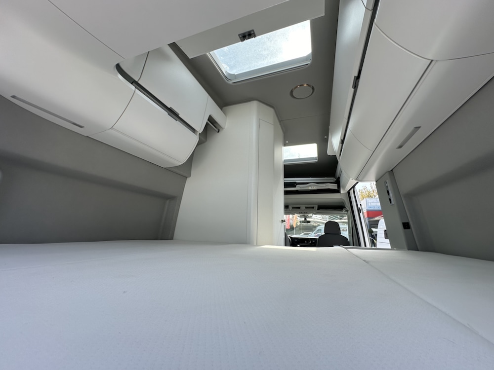 Spacious, modern RV rental bed area featuring overhead storage and skylights, ready for your next adventure.. Volkswagen California 2022