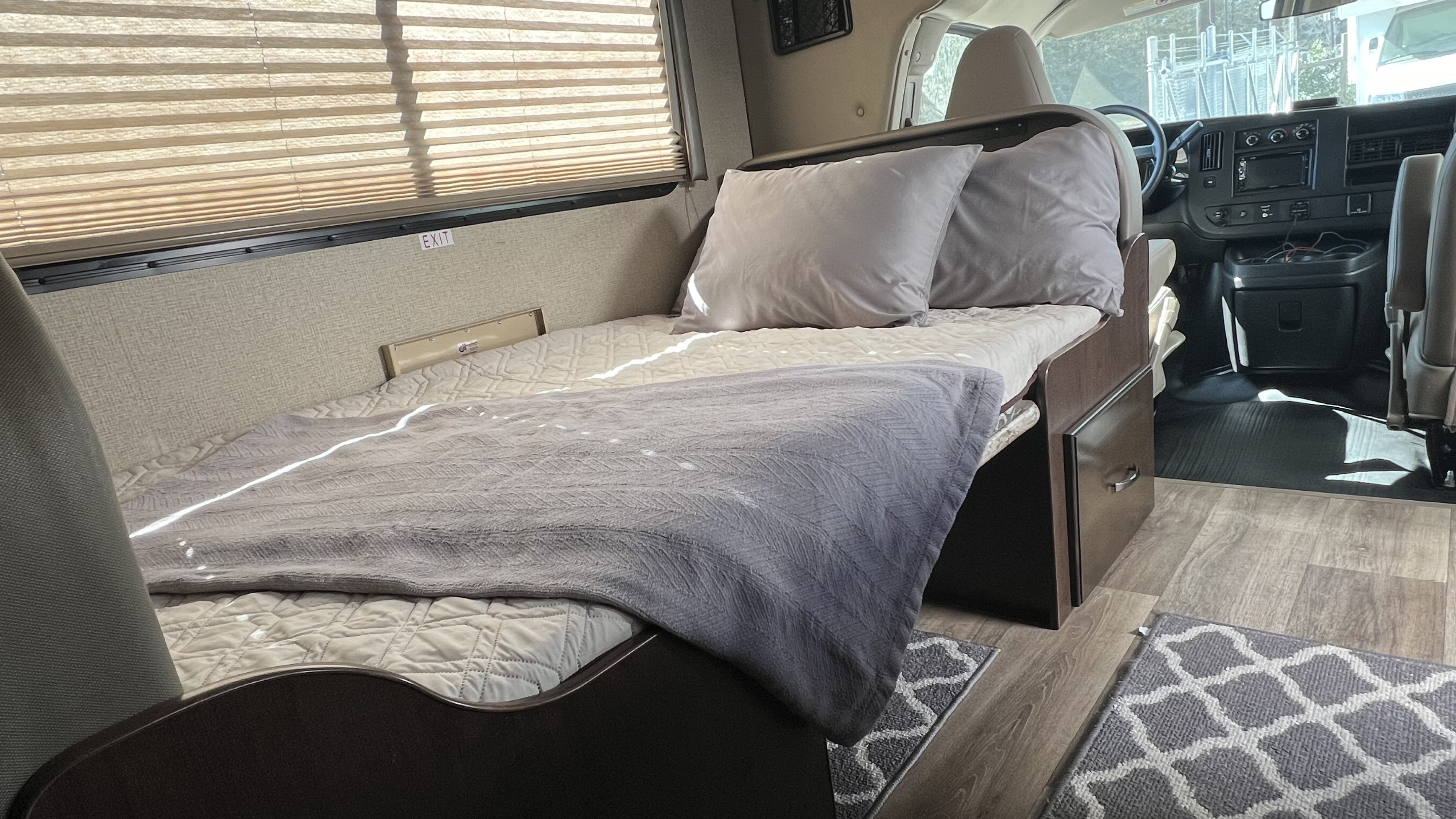 RV rental interior showing a sleeping area with pillows, blankets, window blinds, and the front cab.. Thor 22HE 2019