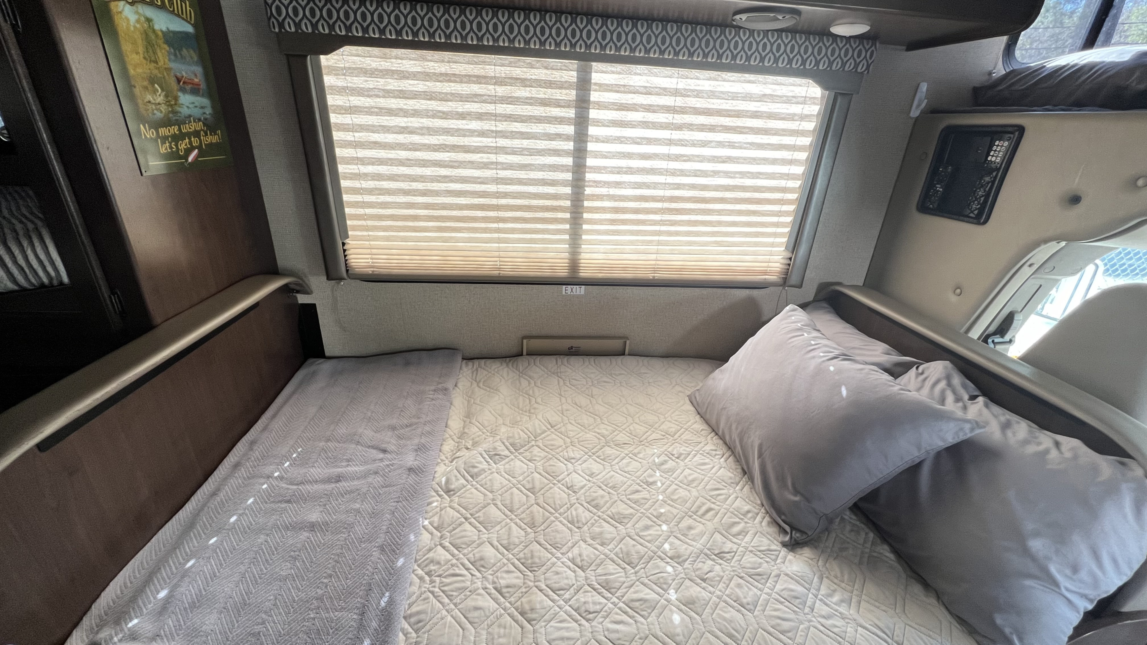 Comfortable sleeping area in an RV rental, featuring a bed, window with blinds, and fishing decor.. Thor 22HE 2019