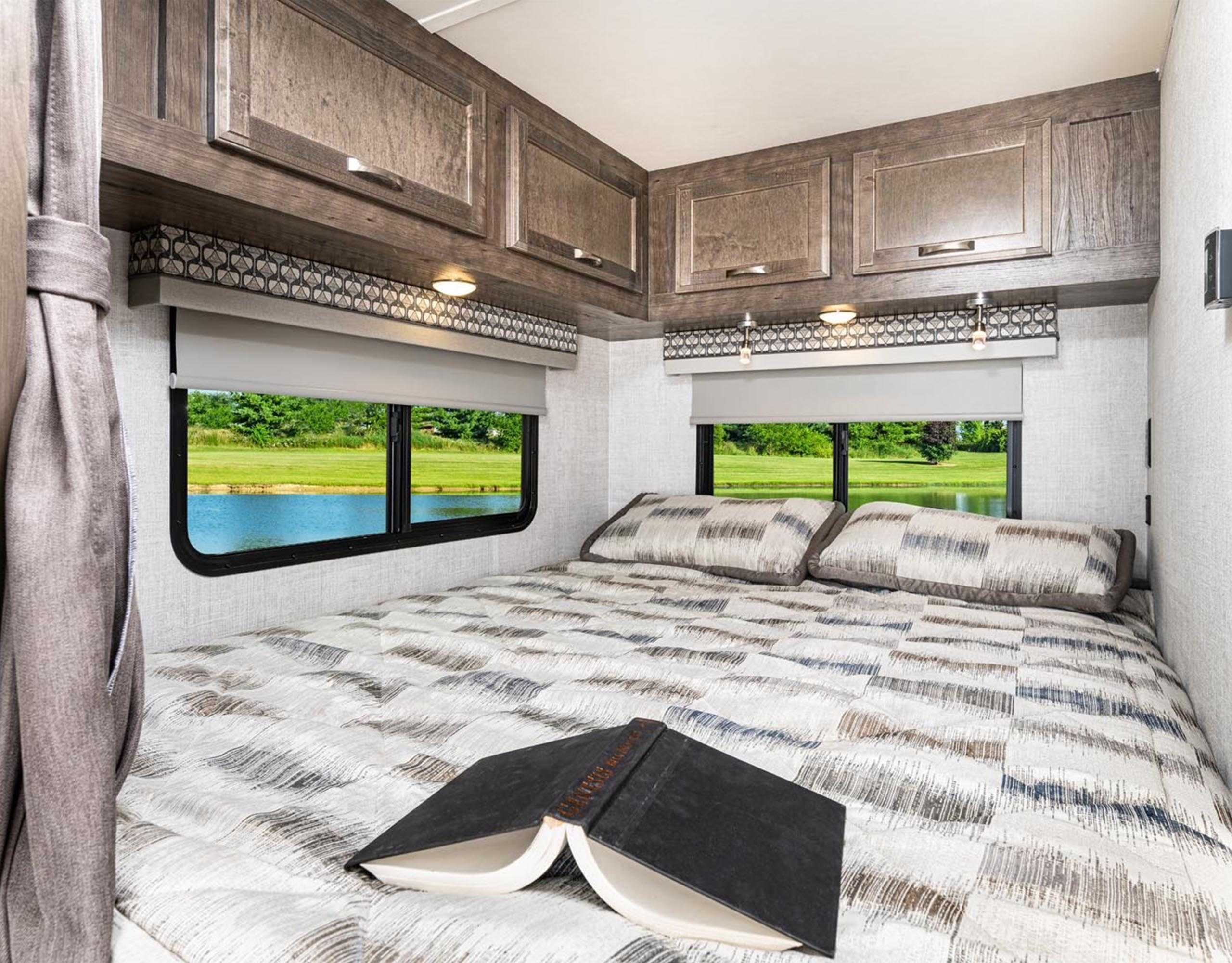 Experience comfort in this RV rental bedroom: cozy bed, ample overhead cabinets, and beautiful lake views. Ideal for mobile adventures.. Gulf Stream Conquest 2021