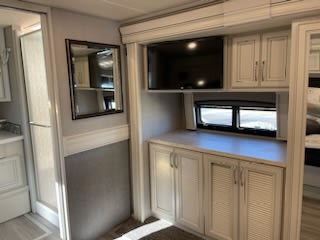 This **RV rental** bedroom interior features a TV, ample storage, and a mirror, with an adjacent bathroom.. Holiday Rambler Navigator 2023