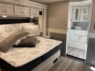 RV rental bedroom with spacious bed, overhead storage, and attached bathroom for travel comfort.. Holiday Rambler Navigator 2023