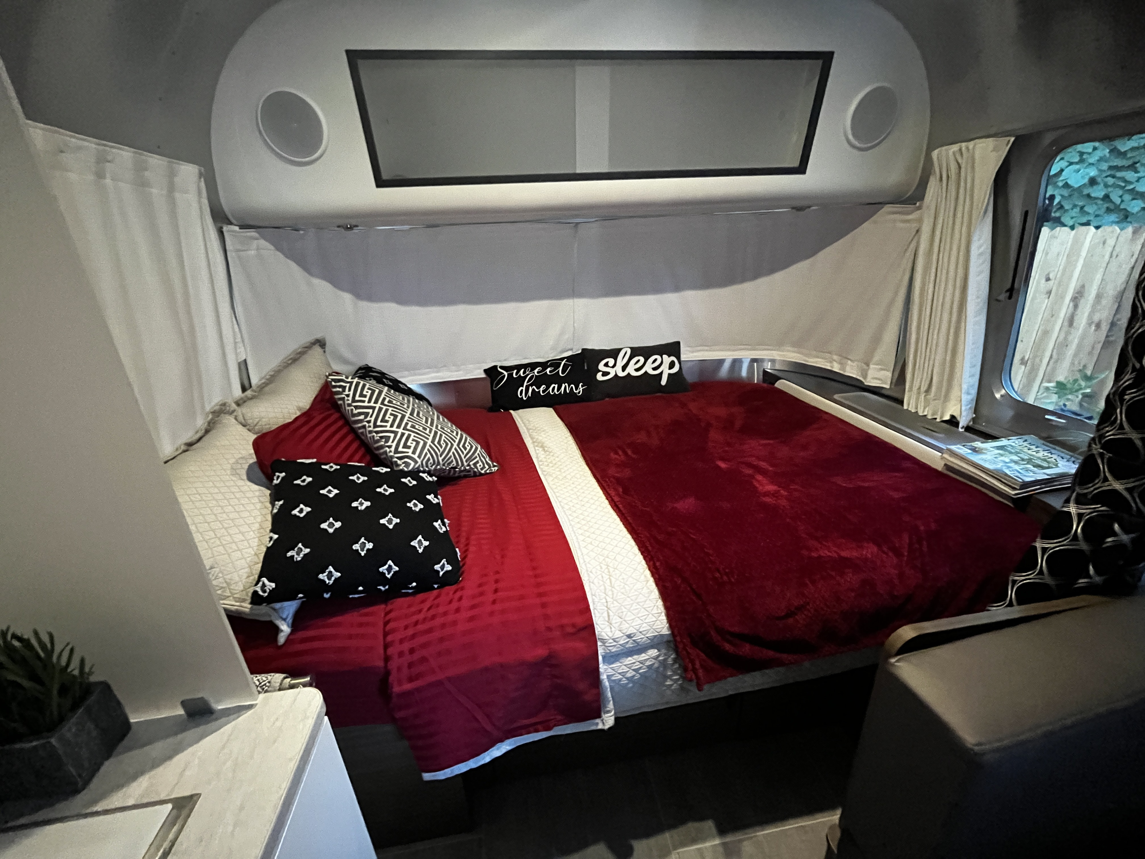 An inviting RV rental bedroom with a large bed, red blankets, patterned pillows, and integrated speakers for a cozy stay.. Airstream Caravel 2021