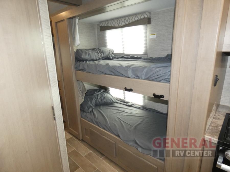 Inside an RV rental: light-toned bunk beds with grey bedding, a window with blinds, and compact cabinetry for travel.. Thor Quantum SE 2022
