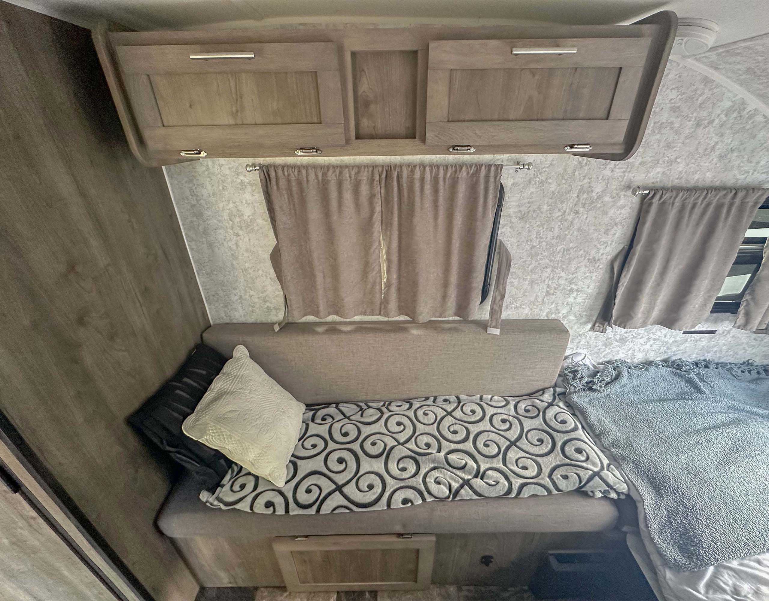 Cozy RV rental interior featuring wooden overhead cabinets, gray curtains, and bench seating with pillows.. Prolite Plus S 2021