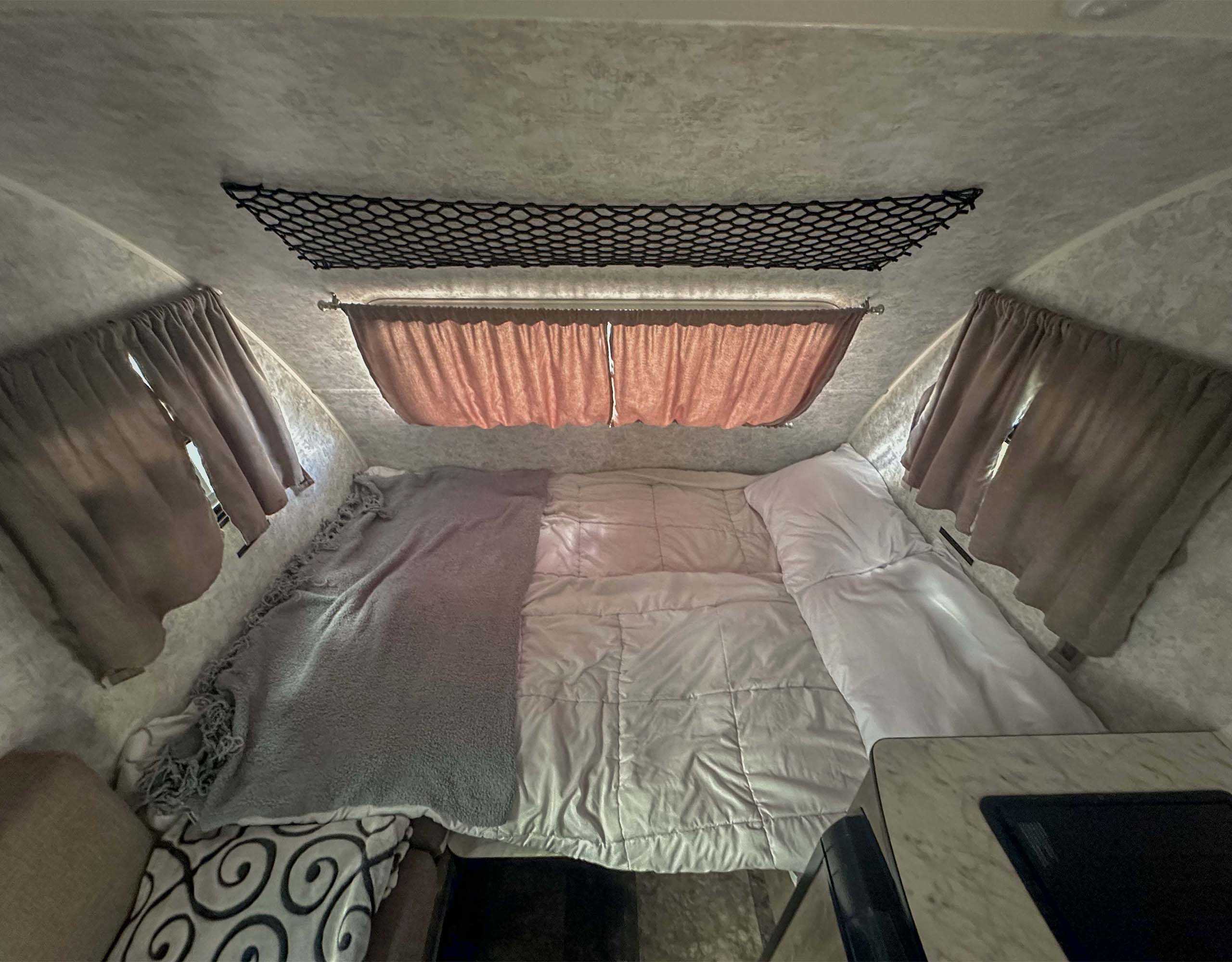 Cozy RV rental bedroom with compact bed, overhead storage net, and curtains. Ideal compact sleeping area.. Prolite Plus S 2021