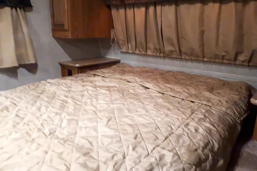 Cozy RV rental bedroom interior, featuring a quilted bed, window curtains, and functional built-in storage.. Forest River Rockwood Mini Lite 2012