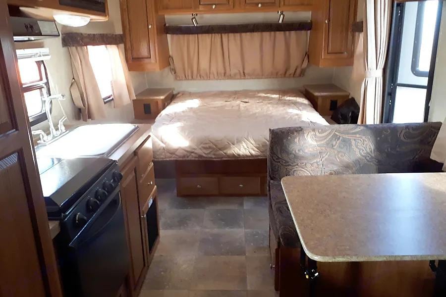 Compact RV rental interior featuring a cozy bed, kitchen with sink & stove, and dinette seating. Perfect for travel!. Forest River Rockwood Mini Lite 2012
