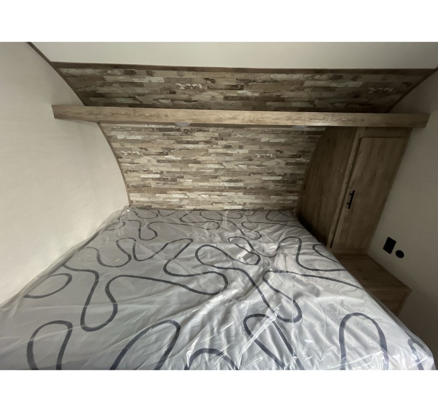 Cozy bed area in an RV rental, featuring a patterned mattress, wood-paneled headboard, and storage.. Gulf Stream Ameri-Lite LE 2024