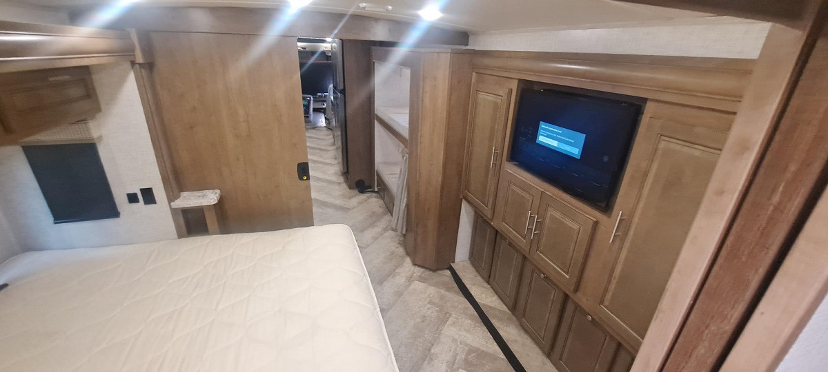 Spacious RV rental interior: bedroom with comfy bed, TV, built-in storage, leading to bunk beds & living area.. Forest River GEORGETOWN 36B5 2021