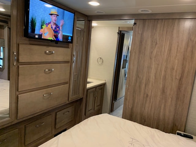 RV rental interior: bedroom with TV above wood dresser, and an open sliding door revealing the bathroom vanity.. Jayco 37TS 2021