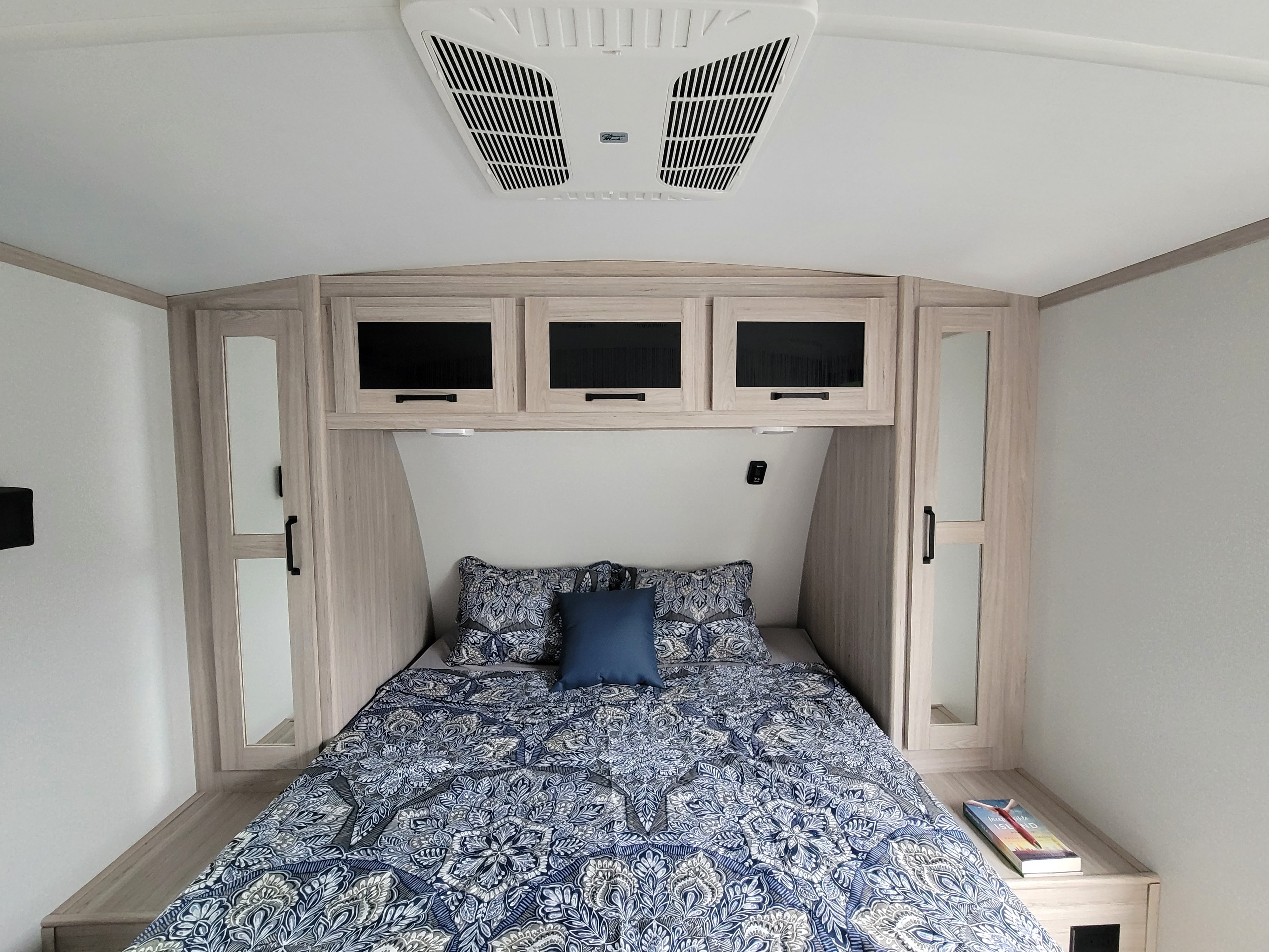 Comfortable RV rental bedroom with patterned blue bedding, ample light wood storage, and ceiling AC unit.. Heartland RVs Sundance Ultra Lite 2022