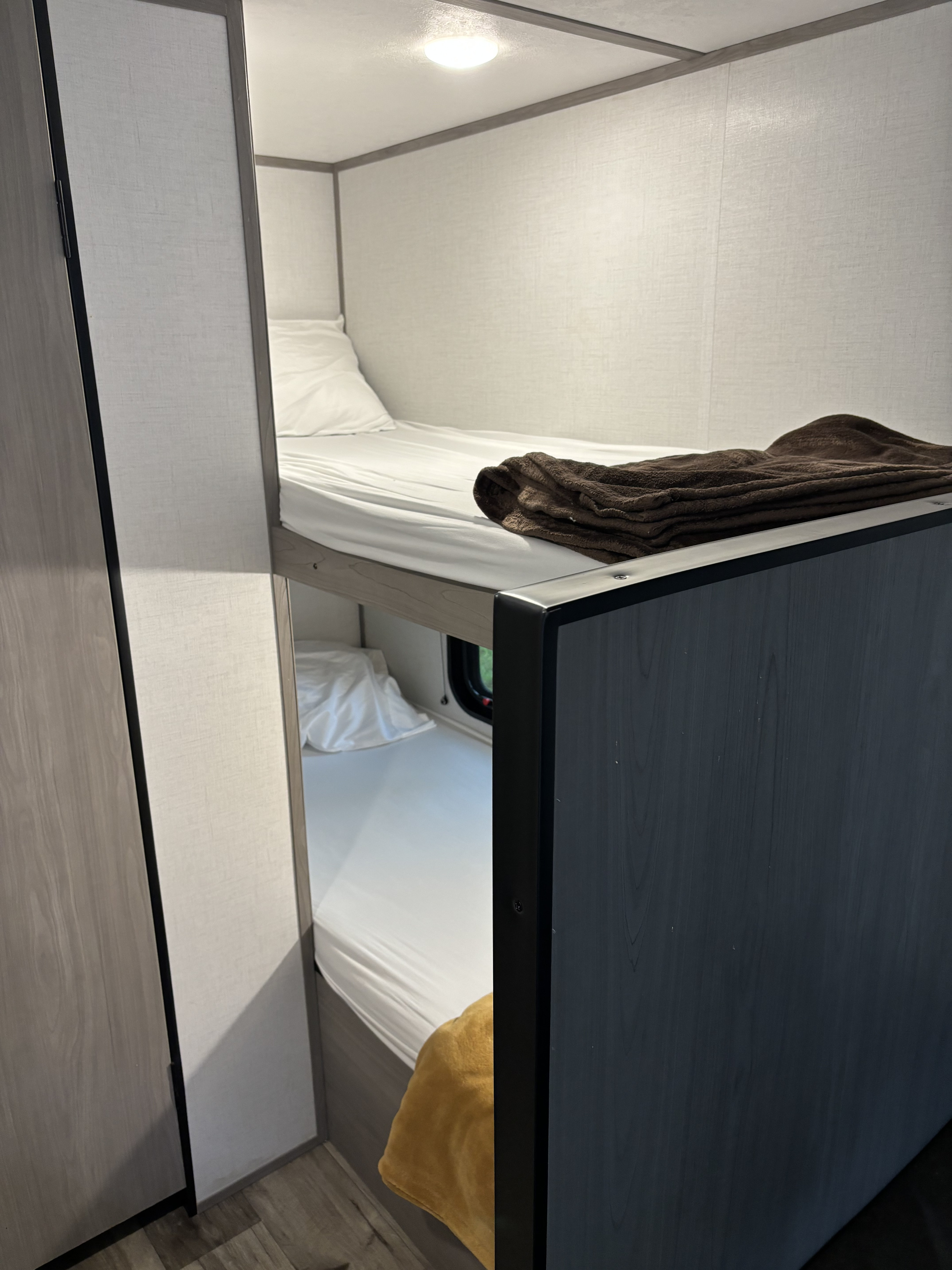 Interior view of an RV rental: cozy, stacked bunk beds with white bedding, ideal for compact travel and sleeping.. Dutchmen Coleman Lantern LT 2023