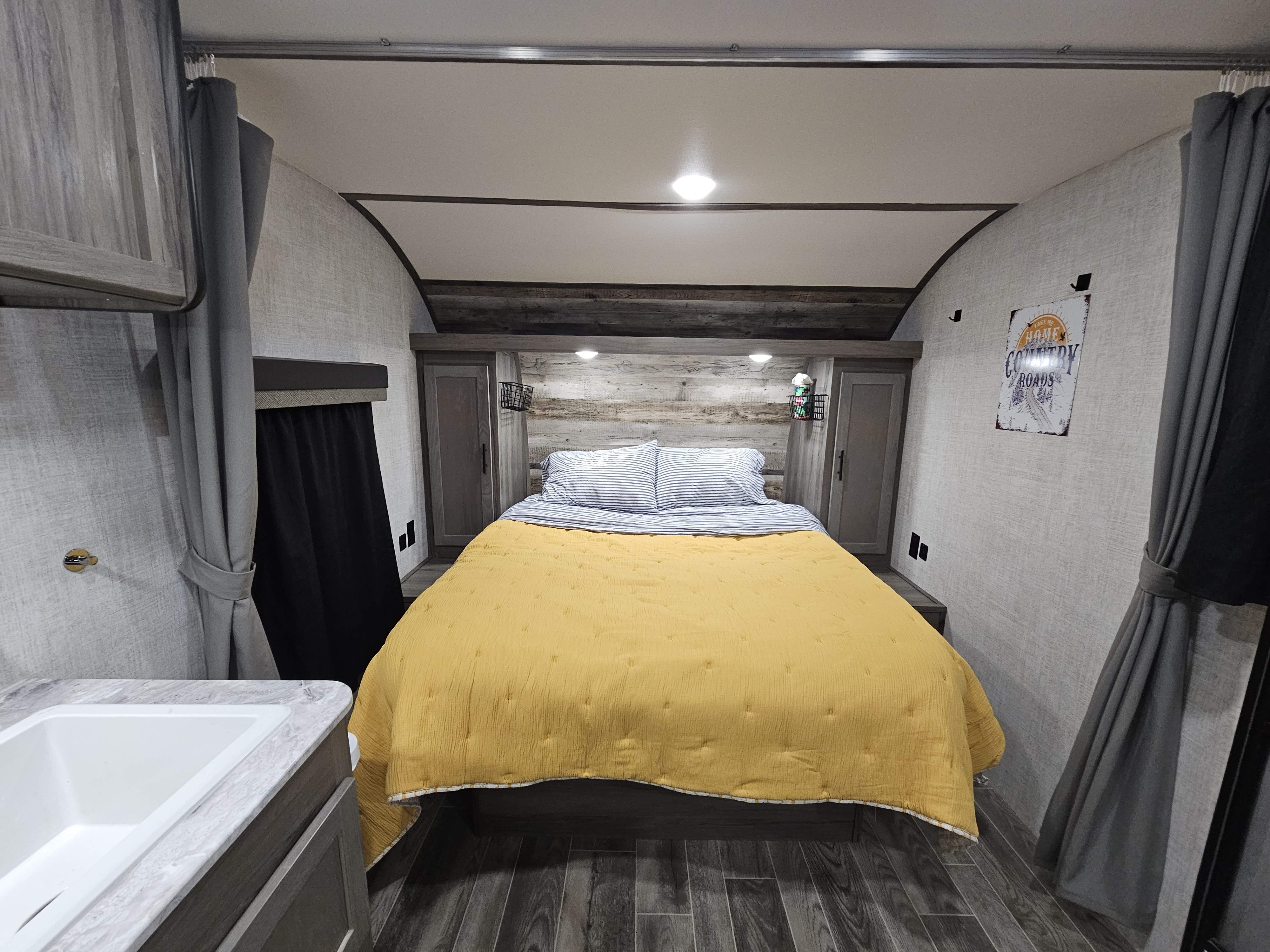 Inviting RV rental bedroom: yellow quilt, striped pillows, and wood-paneled walls. Your comfy travel haven.. Gulf Stream Ameri-Lite 2022