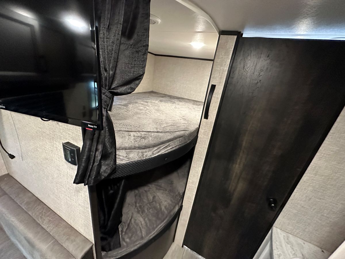 Cozy RV rental interior with bunk beds, a wall-mounted Roku TV, and dark privacy curtains for comfort.. Jayco 264BH 2022