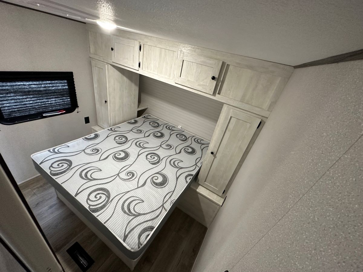 RV rental bedroom showcasing a bed with patterned mattress, ample overhead cabinets, and a window. Cozy interior.. Shasta Oasis 31QB 2024