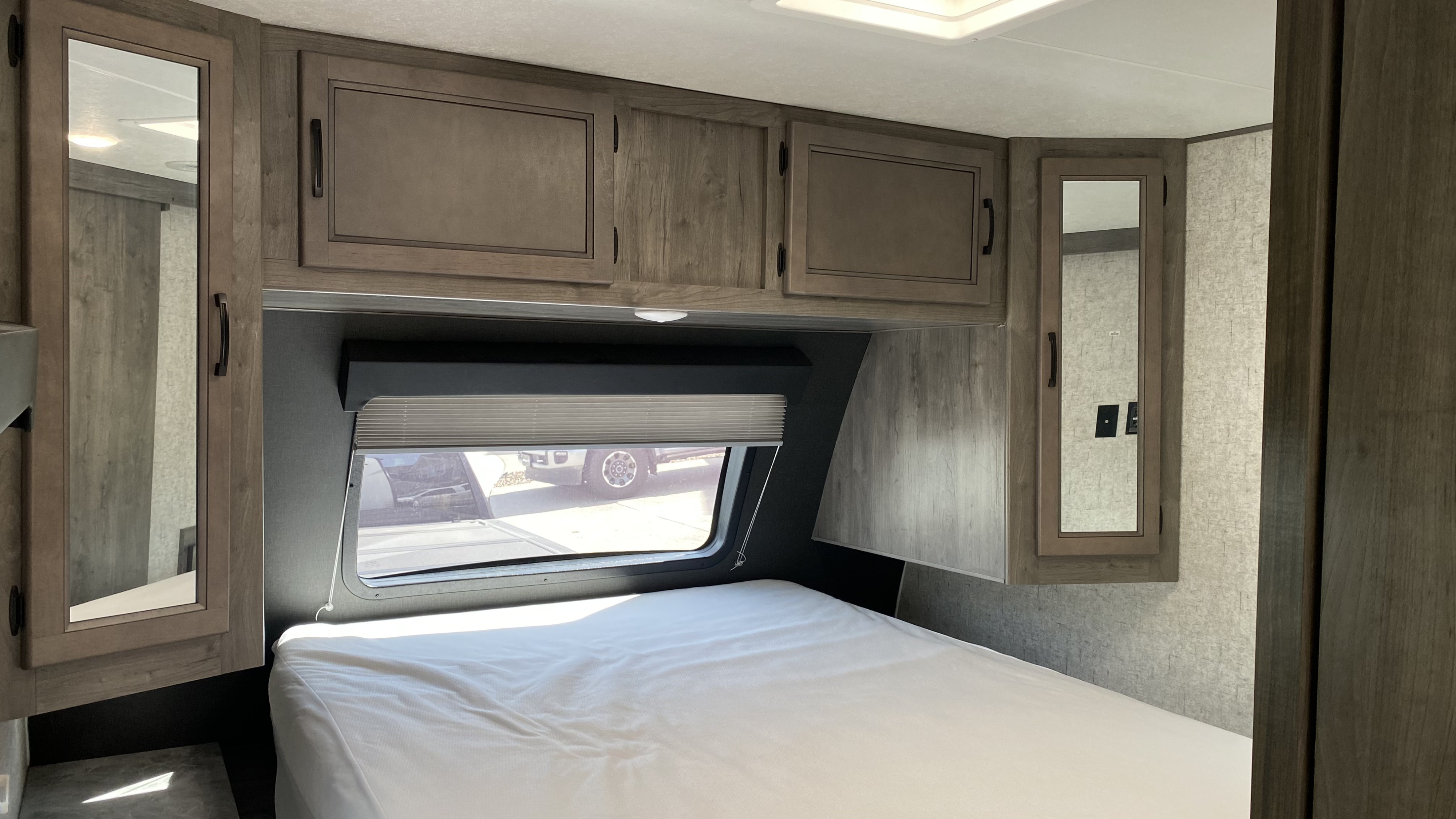 Clean and organized RV rental bedroom featuring a bed, window with blinds, and overhead cabinets.. Coachmen Apex 2020