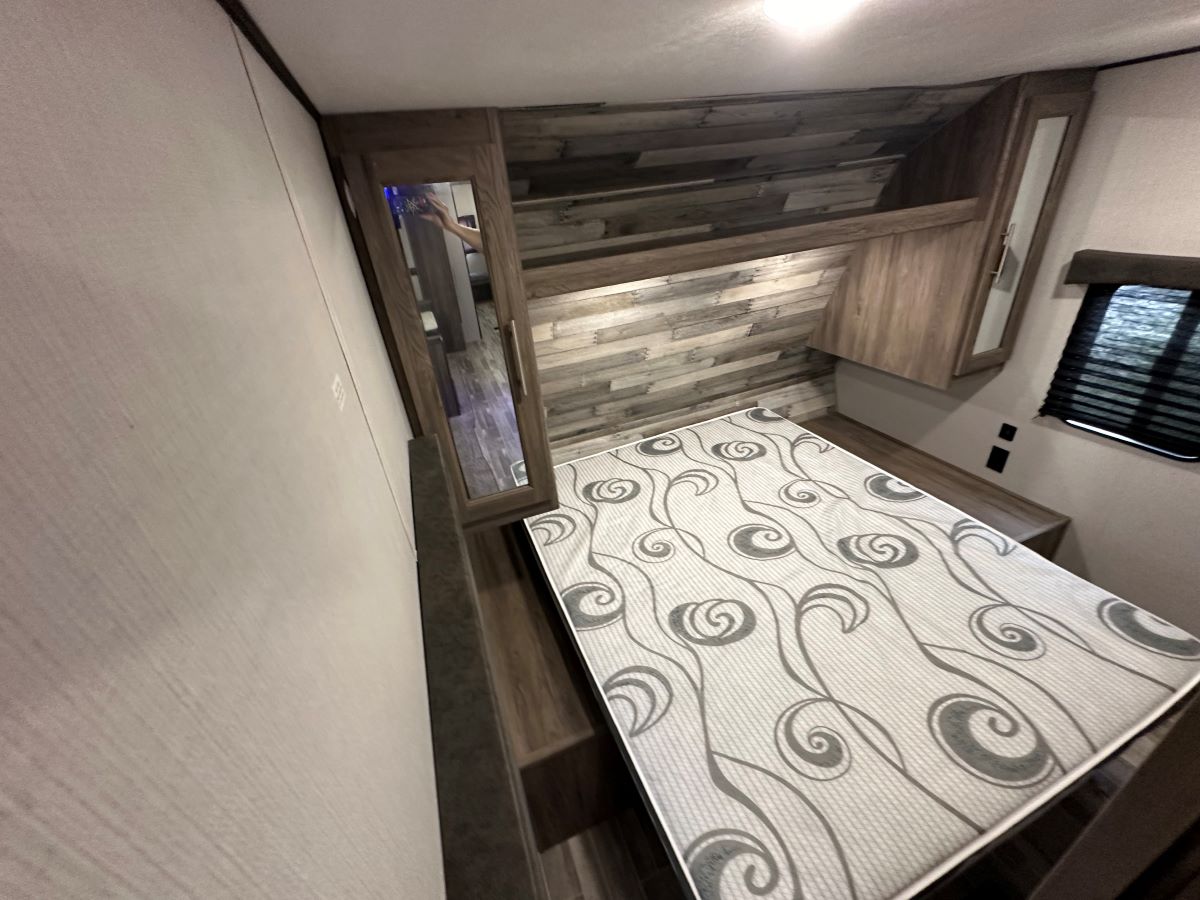 RV rental bedroom showcasing a patterned mattress, mirrored cabinet, overhead storage, and a window with blinds.. Crossroads 328SB 2020