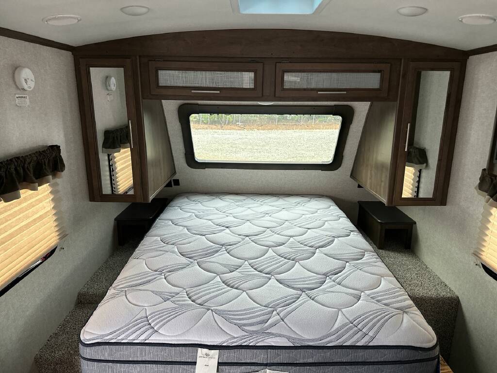 Relax in this RV rental bedroom featuring a large mattress, ample storage, and a window for natural light.. Keystone Cougar Half-Ton 2018