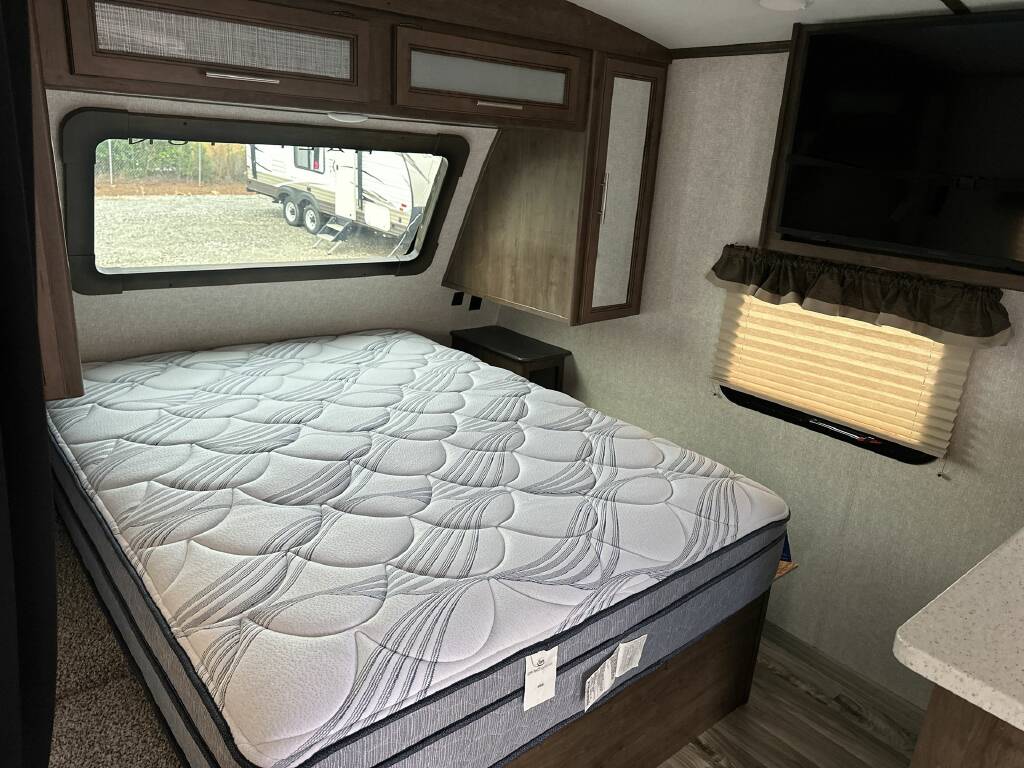 Spacious RV rental bedroom featuring a comfortable bed, large window, and TV. Ideal for travel trailer adventures.. Keystone Cougar Half-Ton 2018