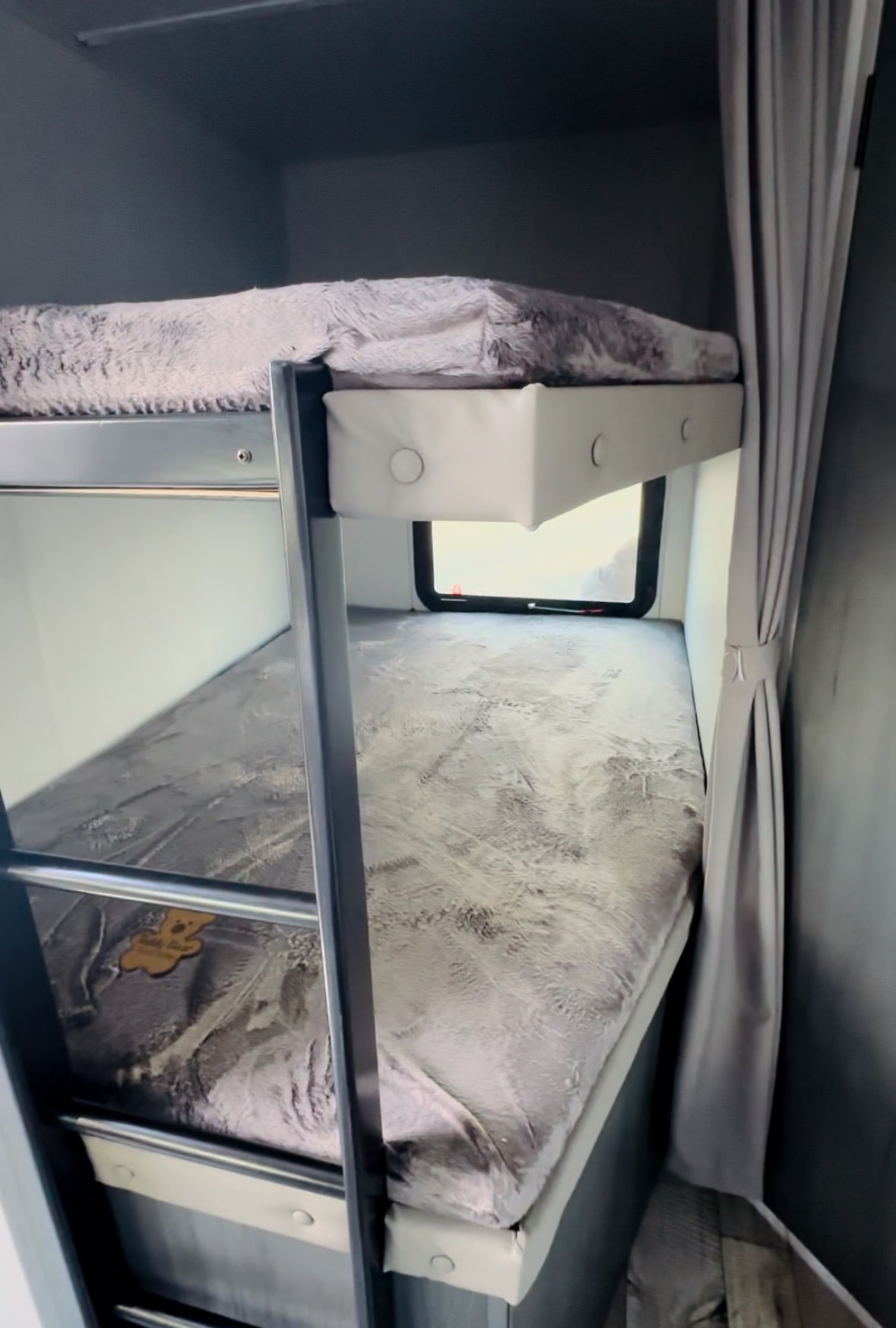 Compact RV rental bunk beds with soft covers and an integrated ladder. Features a small window for natural light, ideal for sleeping.. Aspen Trail Dutchmen 2022