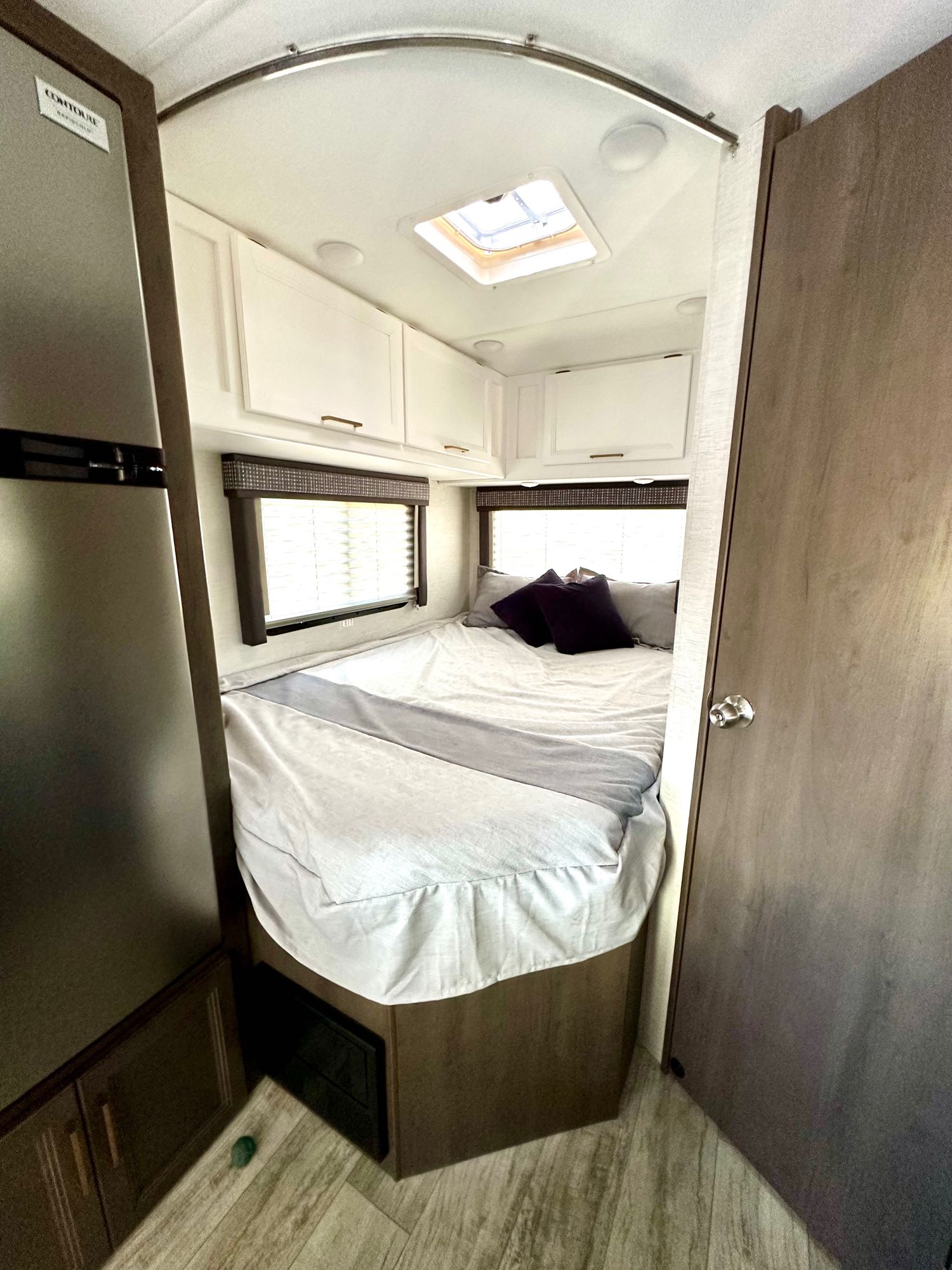 RV rental bedroom view: cozy bed, window, overhead cabinets. A fridge is on the left, perfect for your next trip.. Thor Chateau 2024