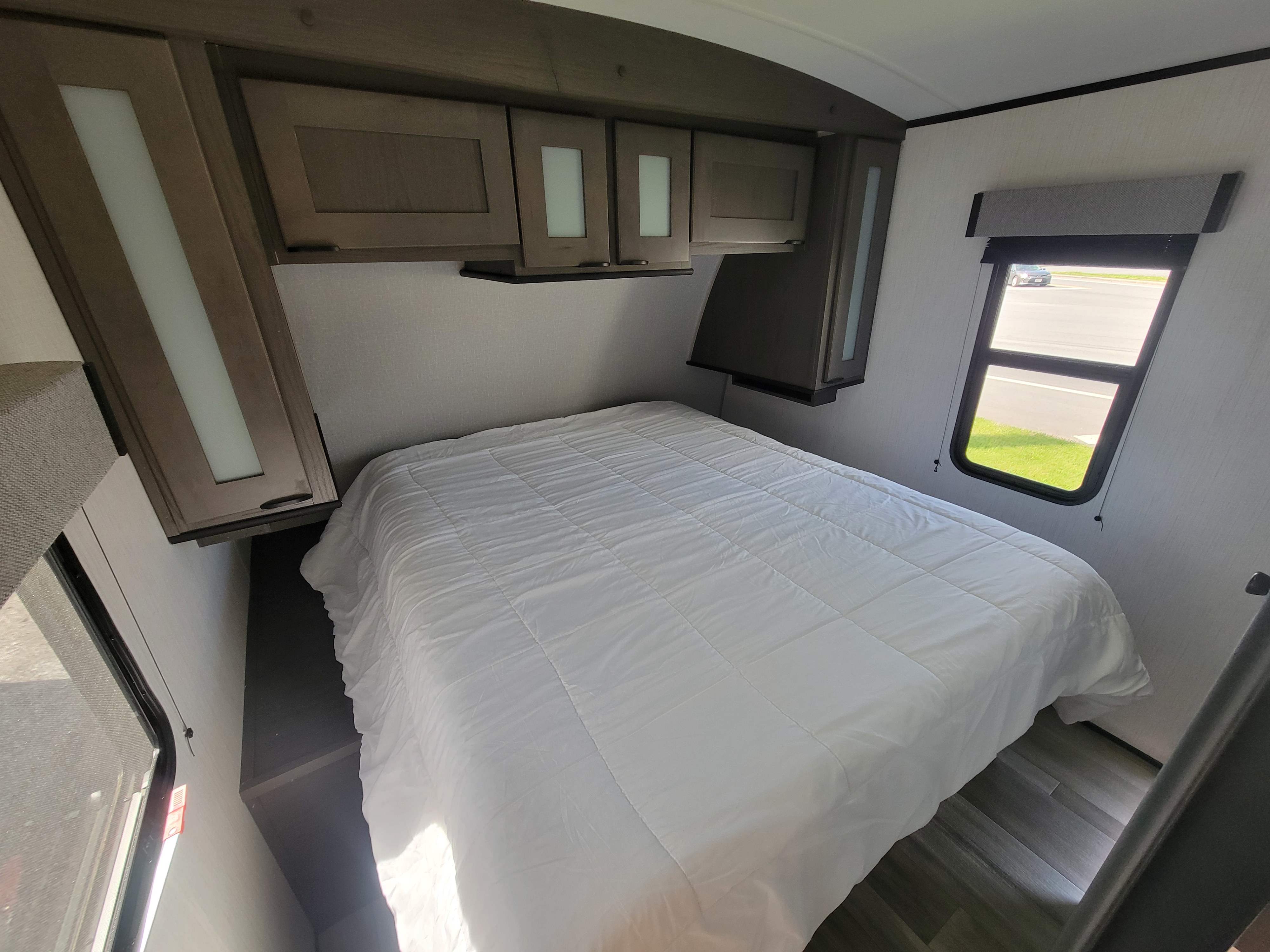 Explore this cozy rv rental bedroom featuring a bed with white comforter, overhead storage, and a window.. Dutchmen Kodiak 2022