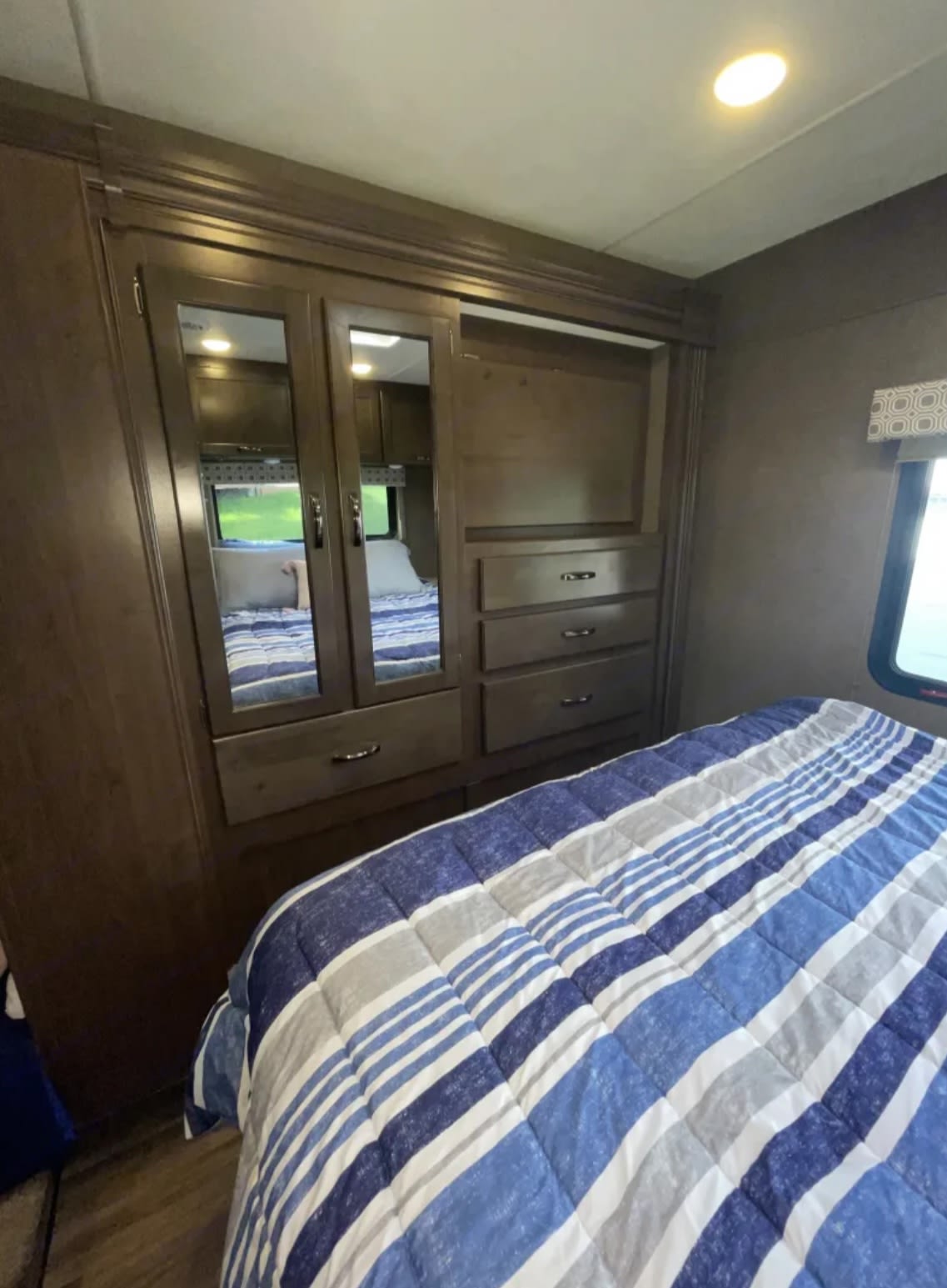Comfortable RV rental bedroom featuring a striped comforter on the bed and a built-in mirrored wardrobe for storage.. Thor Four Winds 2019