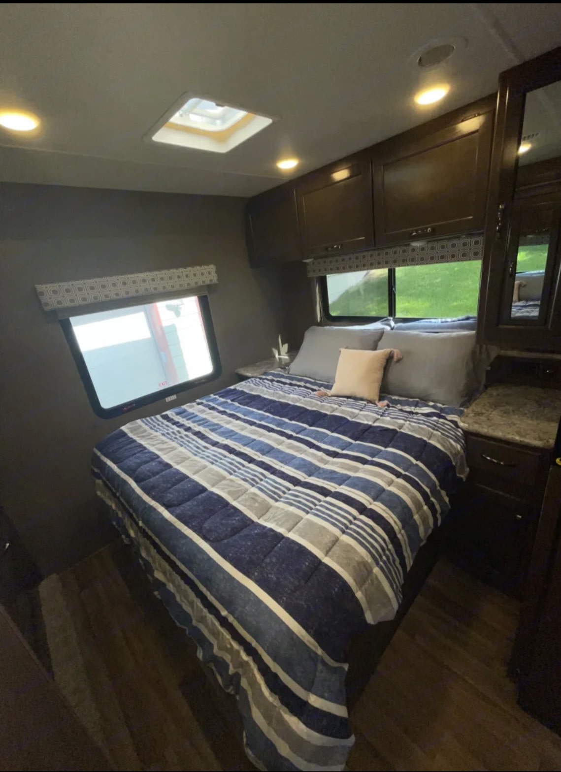 Cozy RV rental bedroom featuring a striped bed, overhead cabinets, windows with natural light, and wood flooring. Perfect for your next trip.. Thor Four Winds 2019