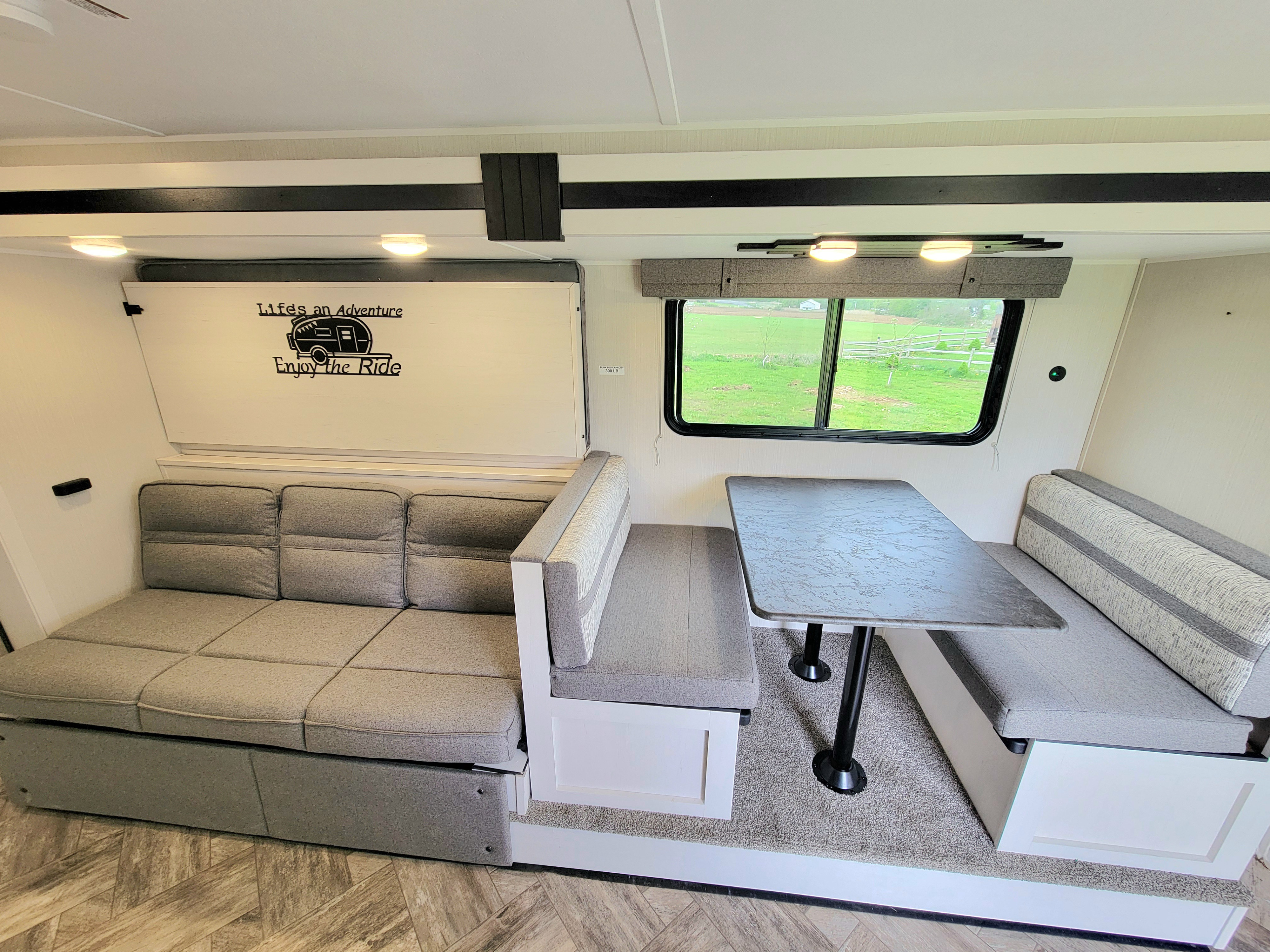 RV rental interior featuring a gray sofa bed, a dinette table with benches, and a window view of green scenery.. Palomino Puma 2023