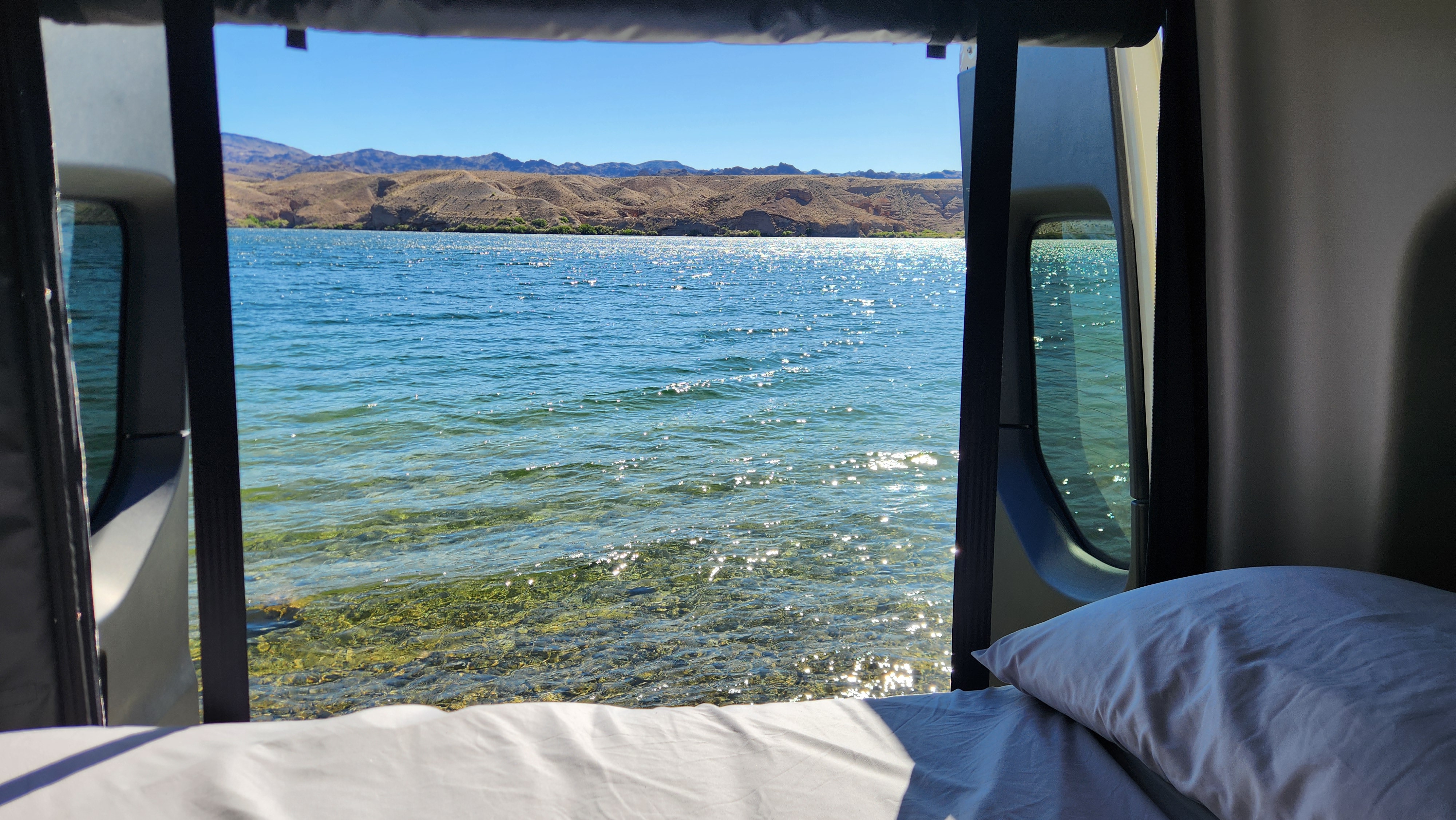 Wake up to stunning lake views from your RV rental bed! Clear water & mountains visible through open rear doors.. Winnebago Revel 2024