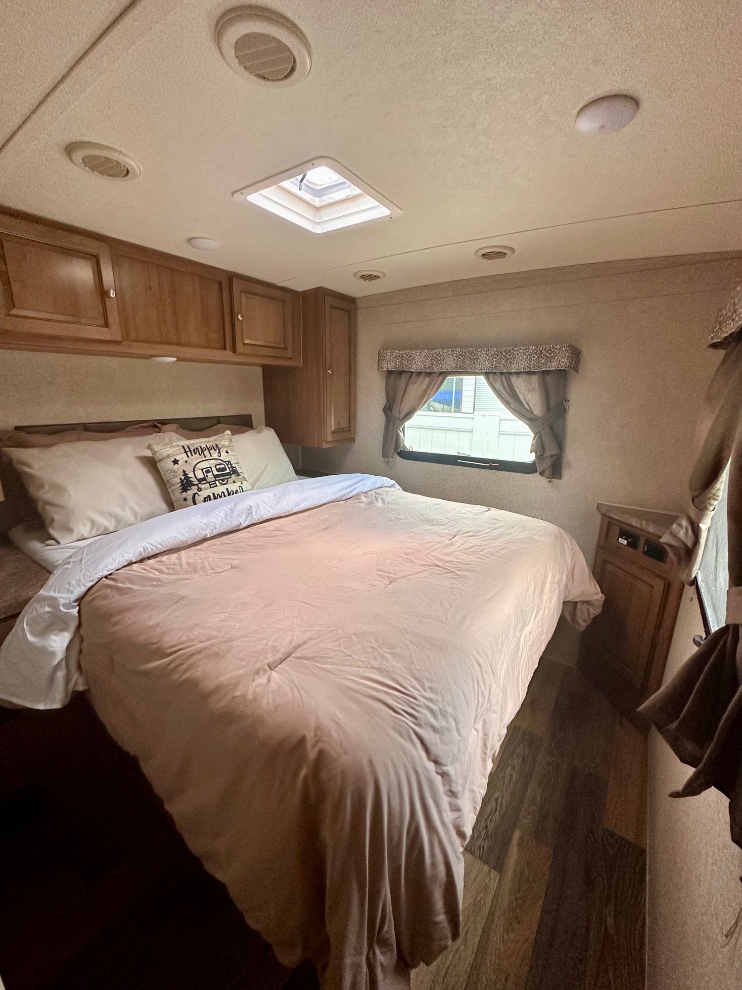 RV rental bedroom with a large, neatly made bed, wooden overhead cabinets, a window, and a ceiling skylight for light.. Forest River Rockwood Mini Lite 2016