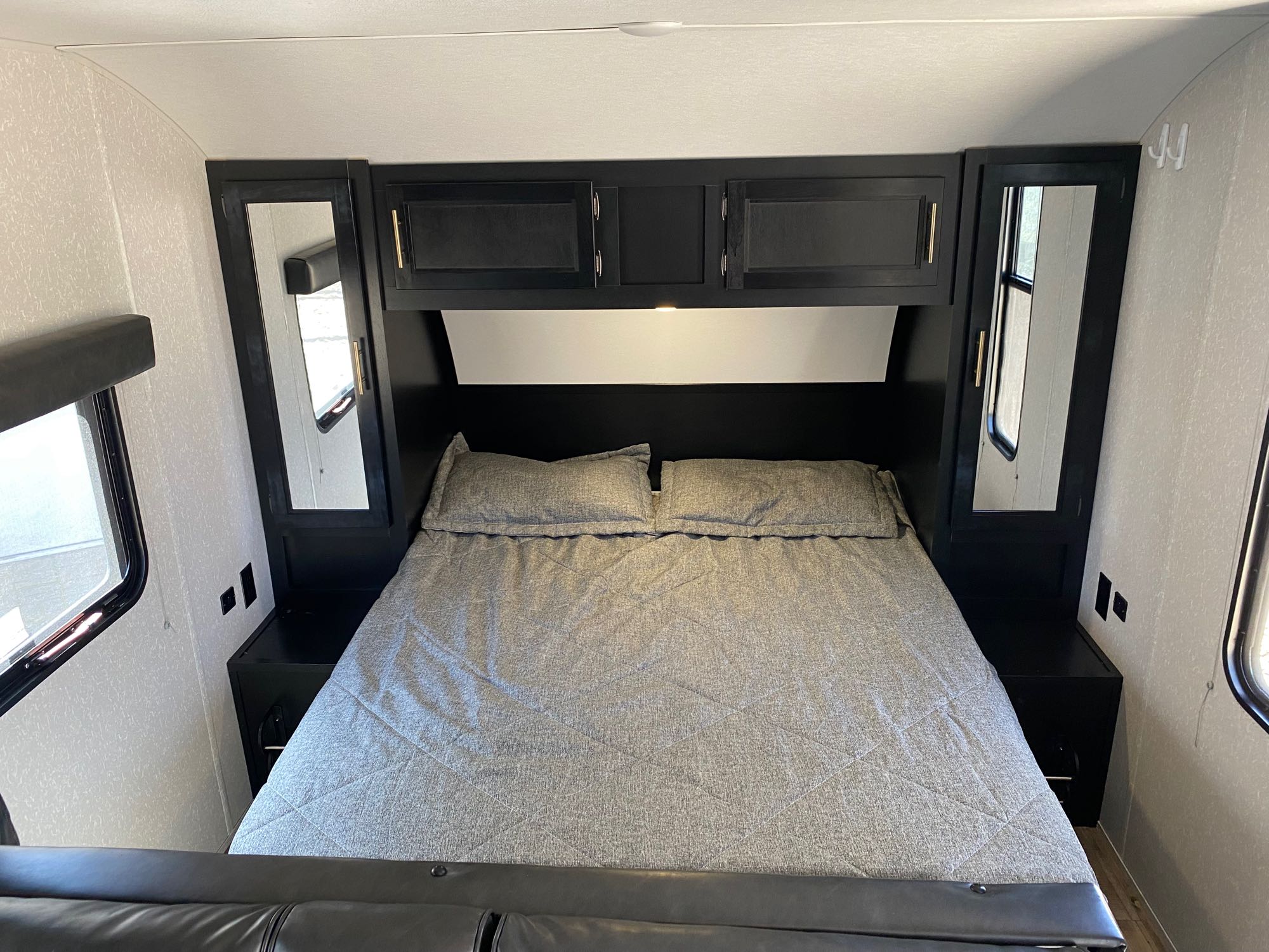 This RV rental bedroom features a comfy bed with gray bedding, overhead cabinets, and side windows for a complete camper experience.. Forest River Cherokee Grey Wolf Special Edition 2022