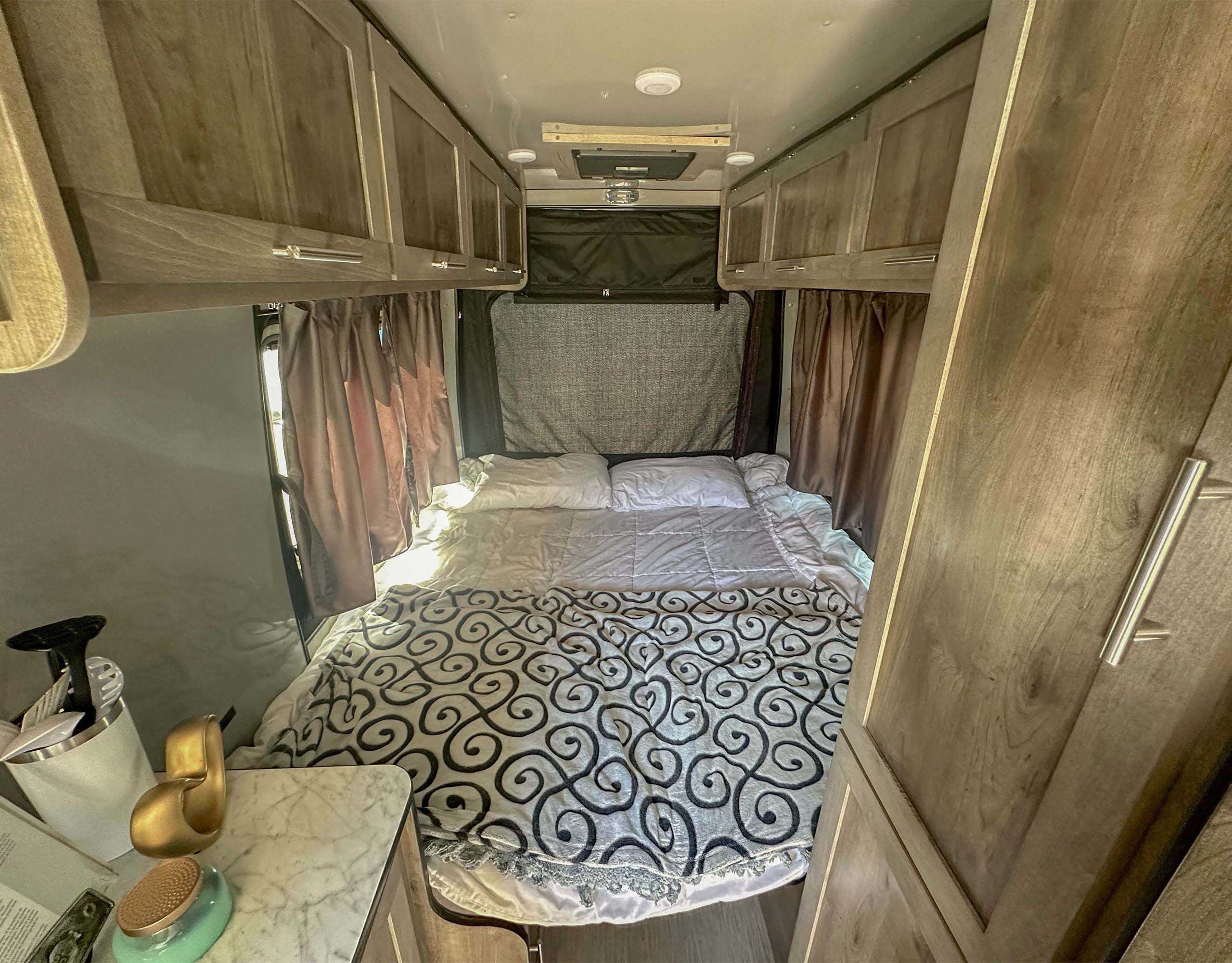 An RV rental's cozy bedroom with a patterned comforter, overhead cabinets, and side counter.. Prolite E-Volution MS21 2024