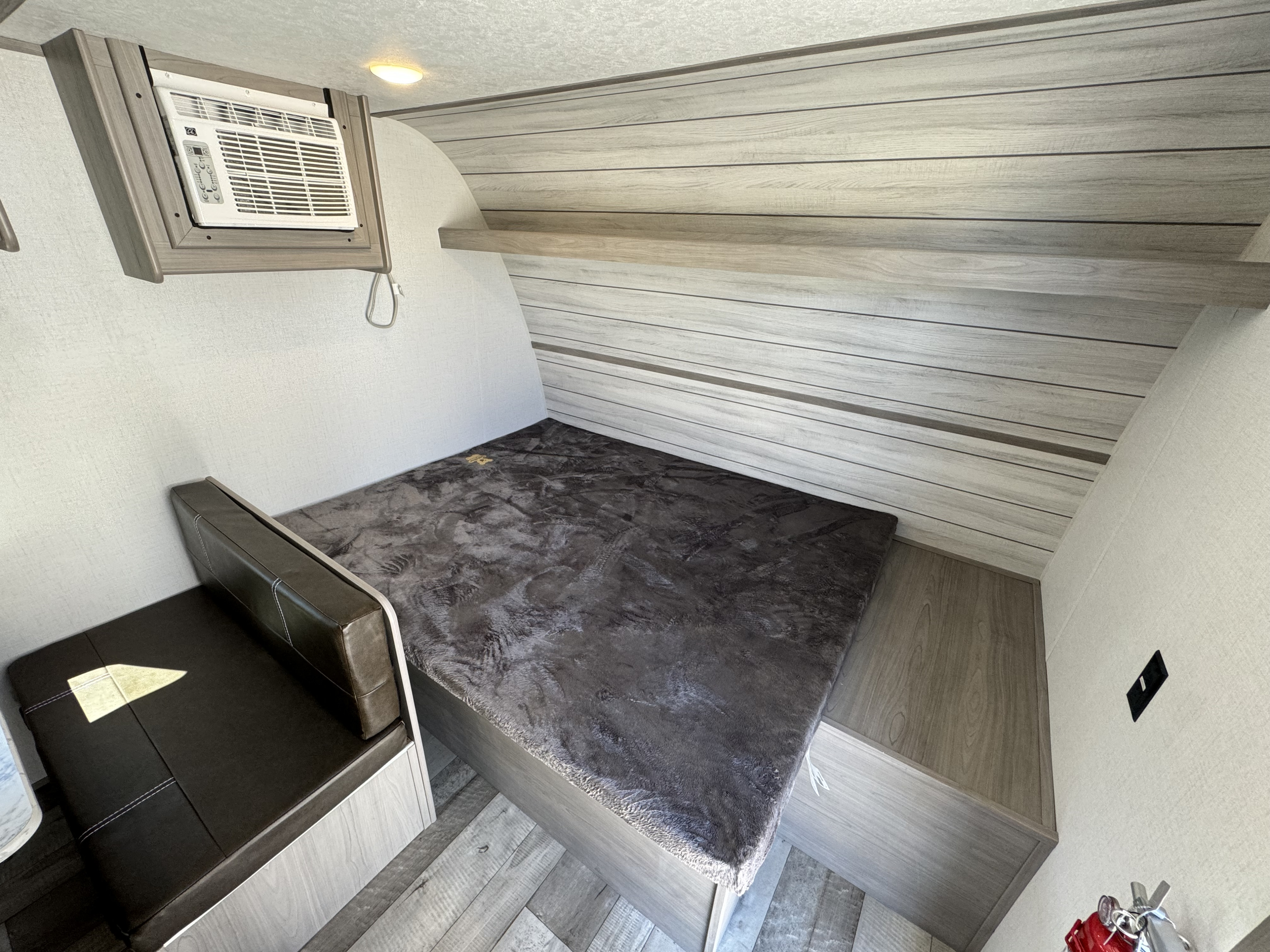 **RV rental** interior: cozy bedroom area with a bed, small bench, AC unit, and wood-look walls.. Keystone RV Coleman 17b 2024