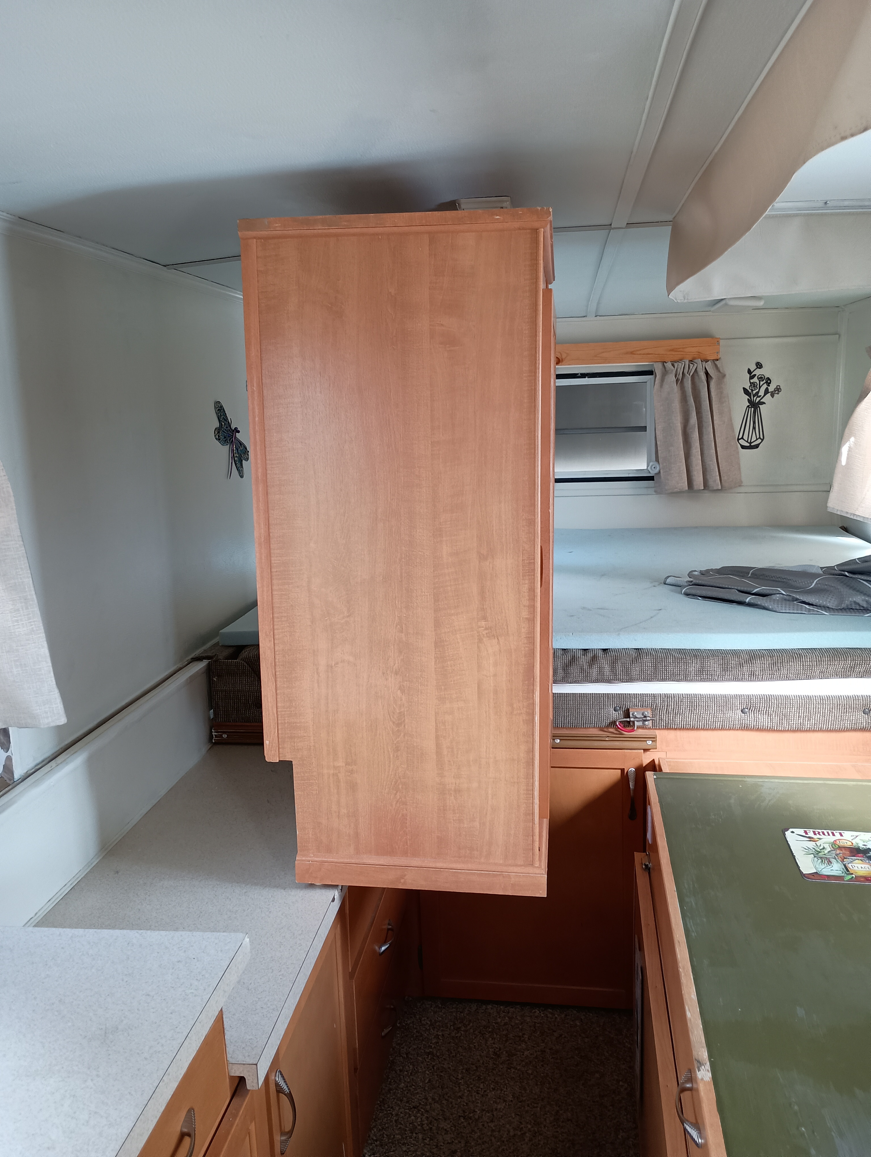 Inside an RV rental: a light wood cabinet, speckled countertops, a green tabletop, and a cozy bed with window.. Trailmanor Trailmanor Trailer 2005